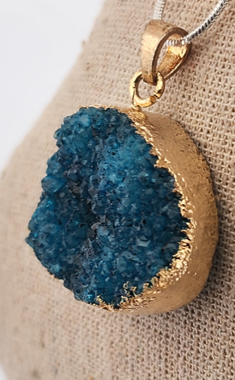 Gold pendant with blue geode on a beige fabric background