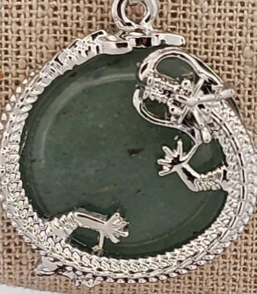 Silver pendant with green stone and lizard design on a textured background