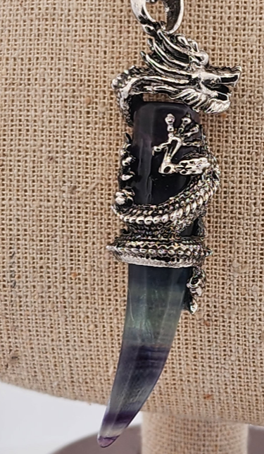 Pendant with black stone and silver dragon design on a textured beige background