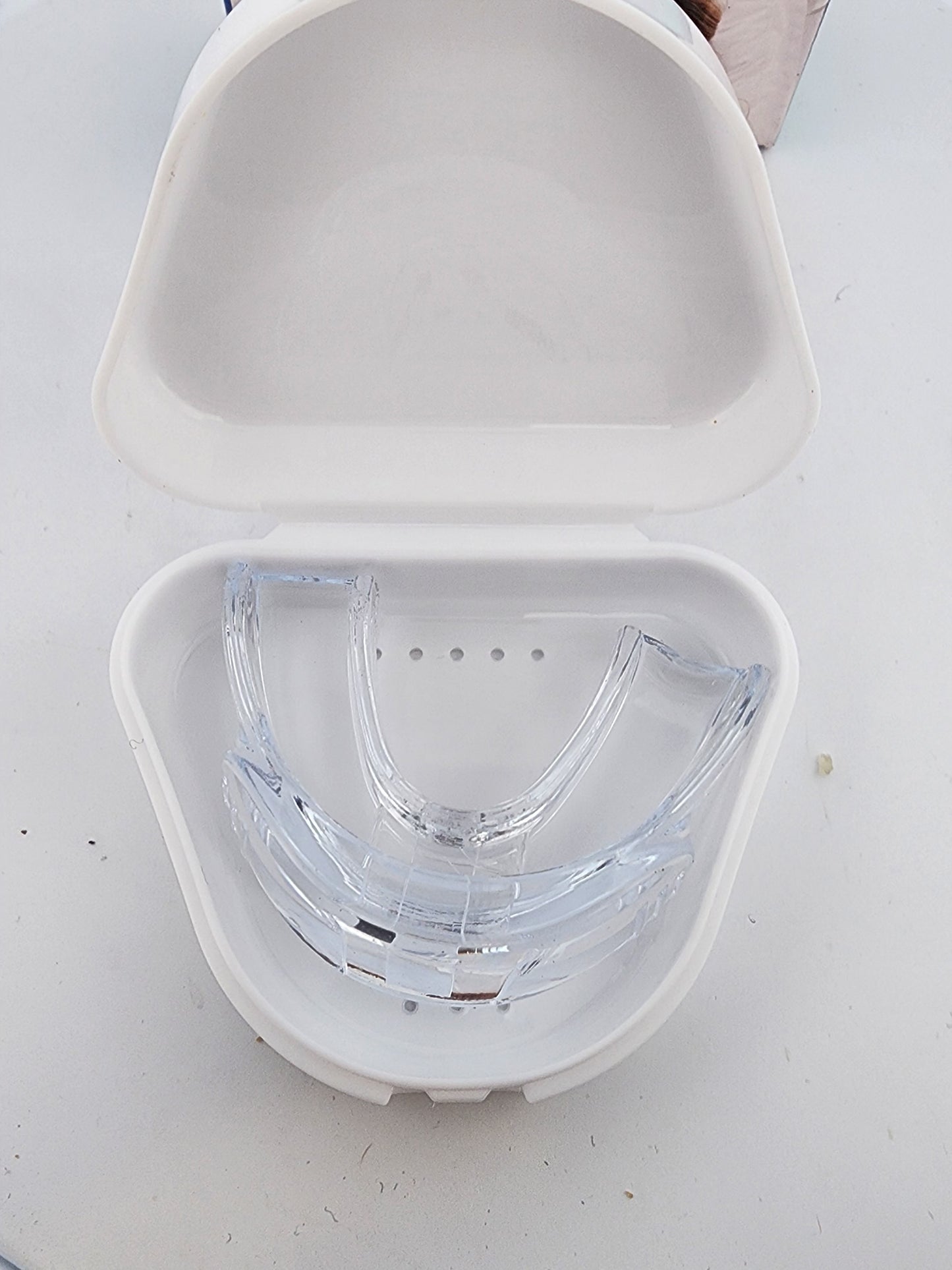 Clear dental aligner in a white case on a light gray background