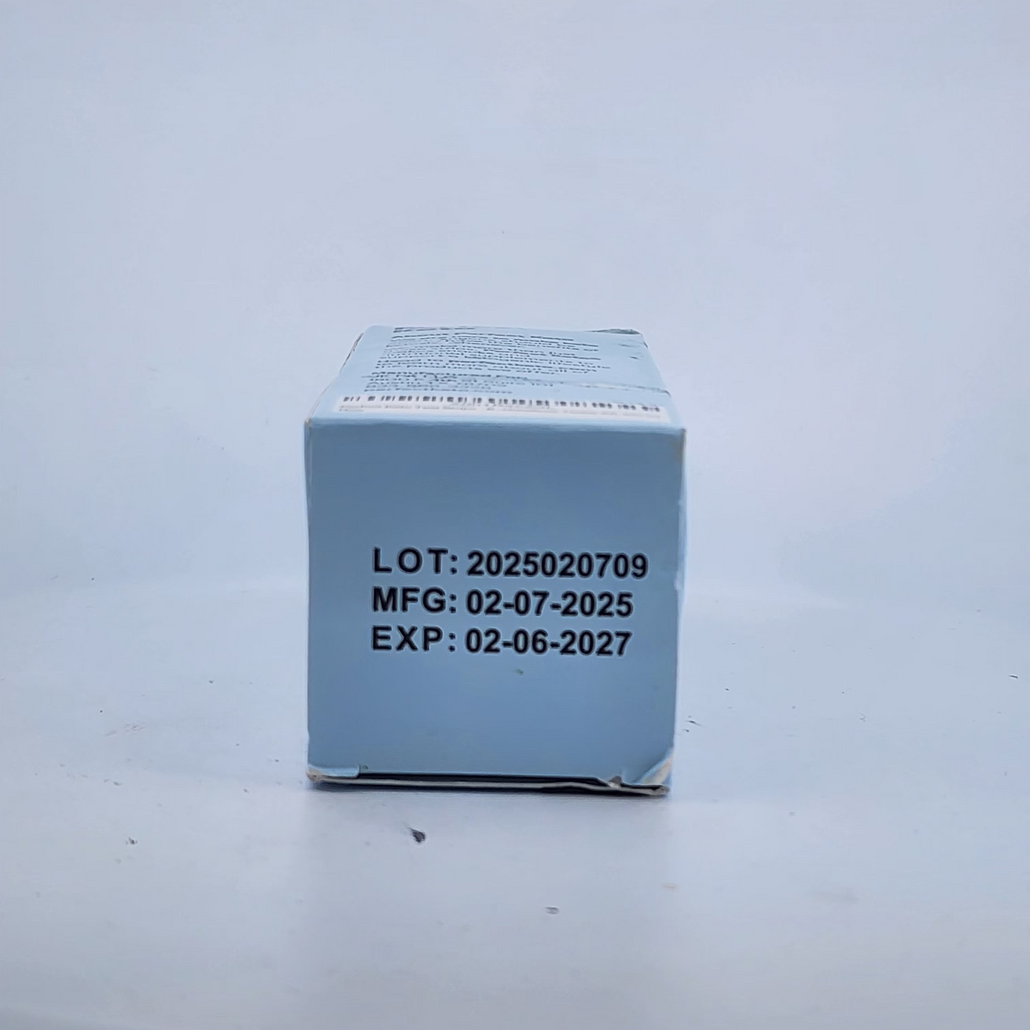 Cube-shaped box with batch, manufacturing, and expiration dates on a light gray background