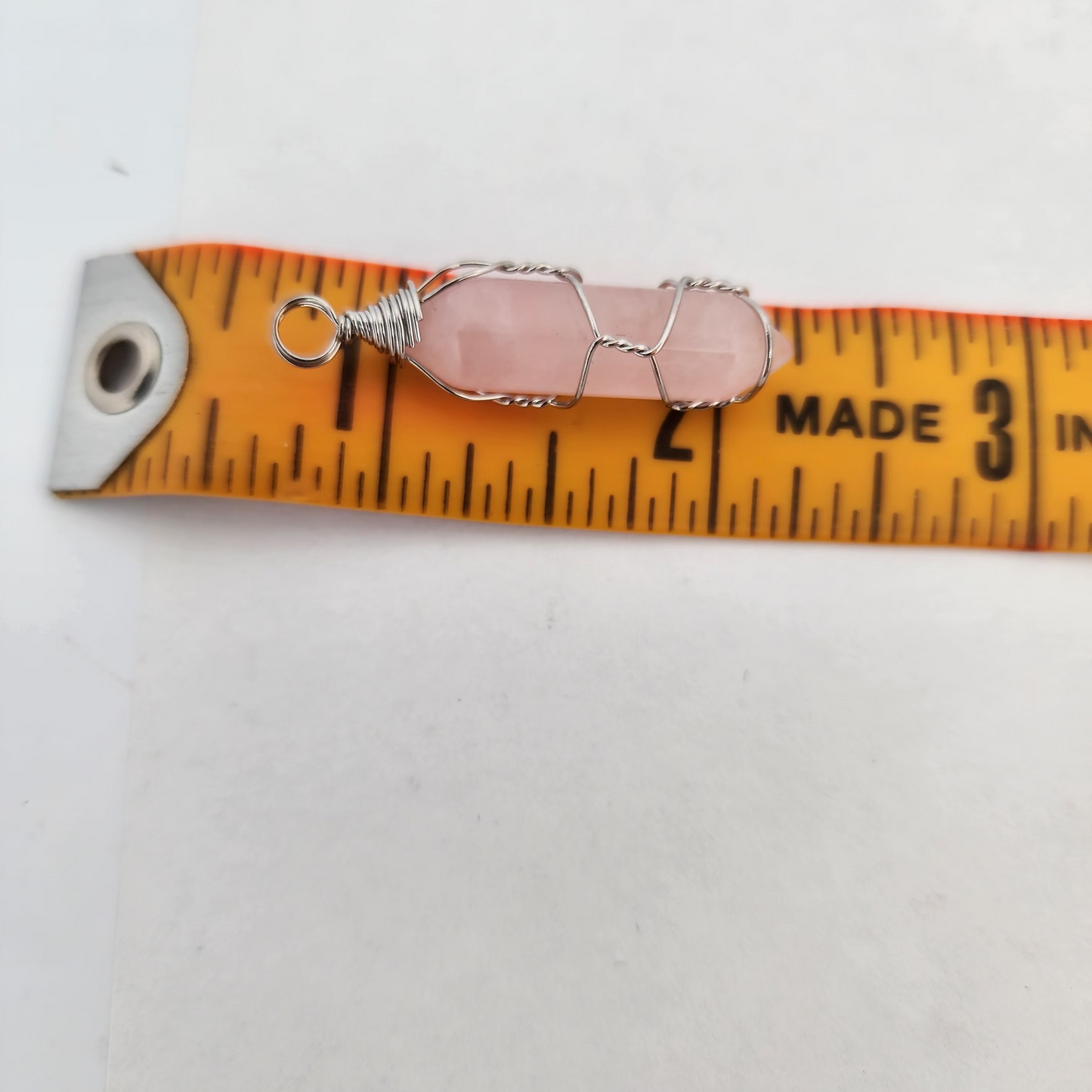 Small silver pendant with a pink stone on a measuring tape against a white background