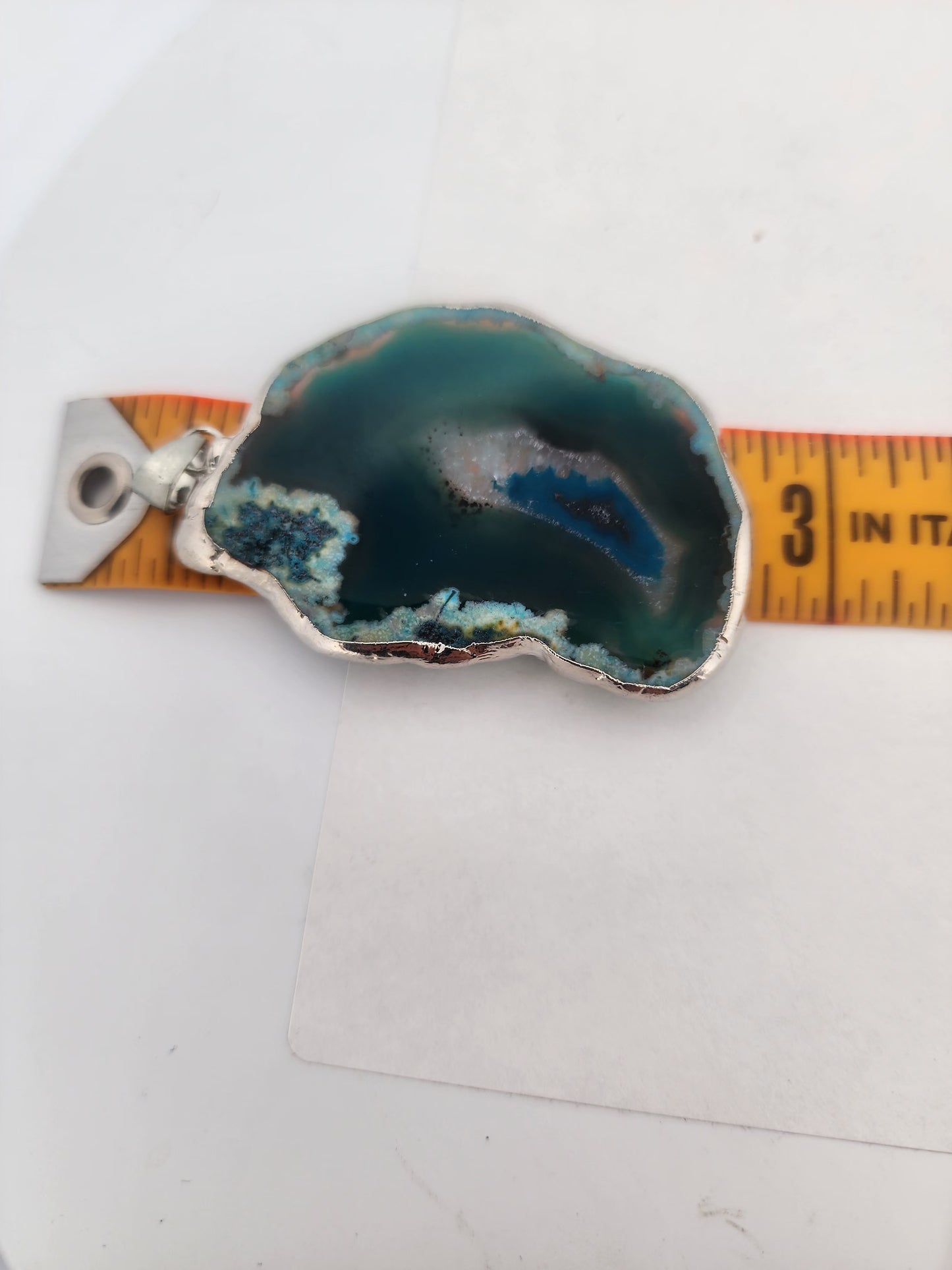 Geode crystal pendant with silver base on a white background, measured by a ruler.