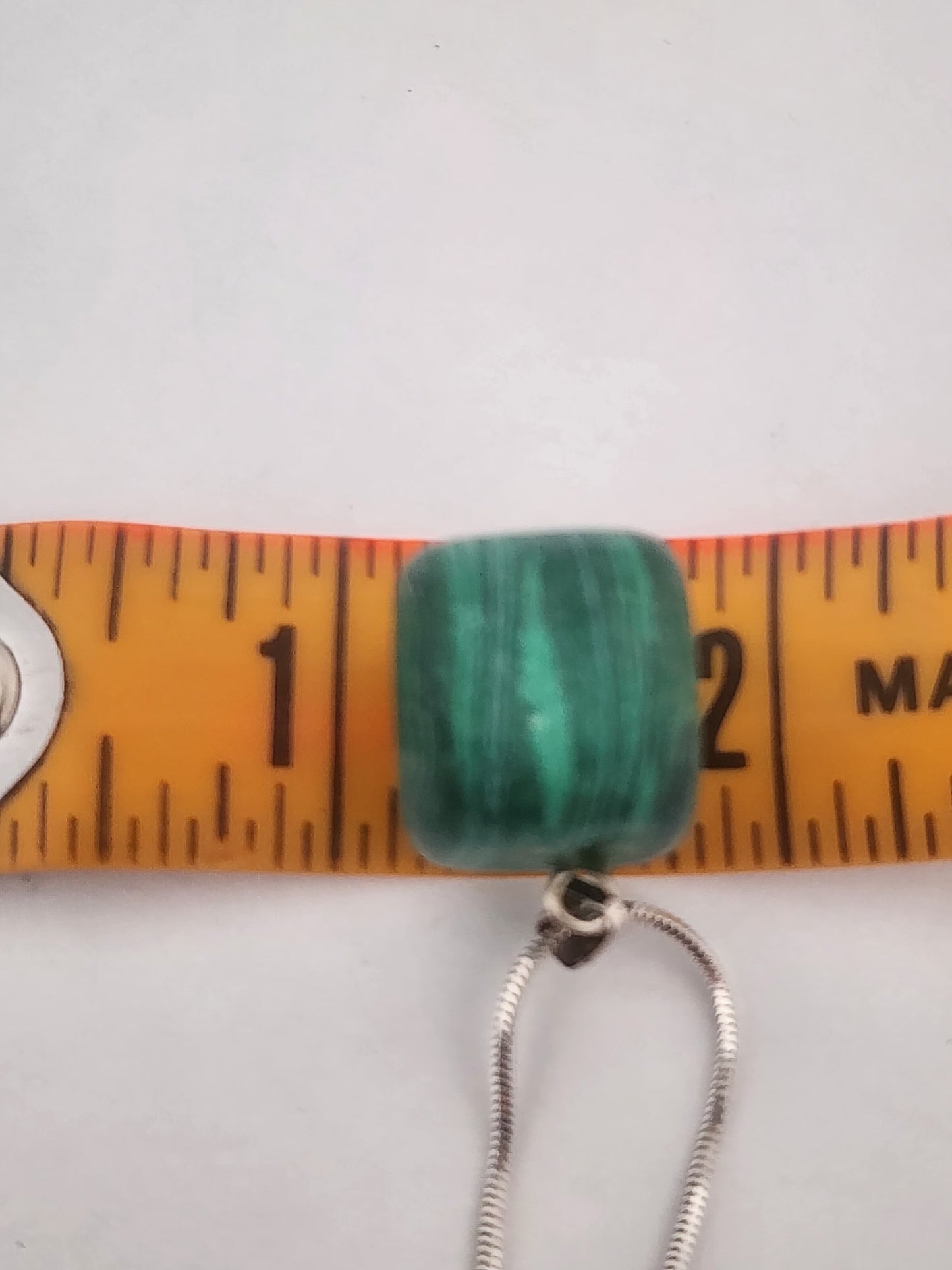 Green beaded necklace with a measuring tape for scale on a white background