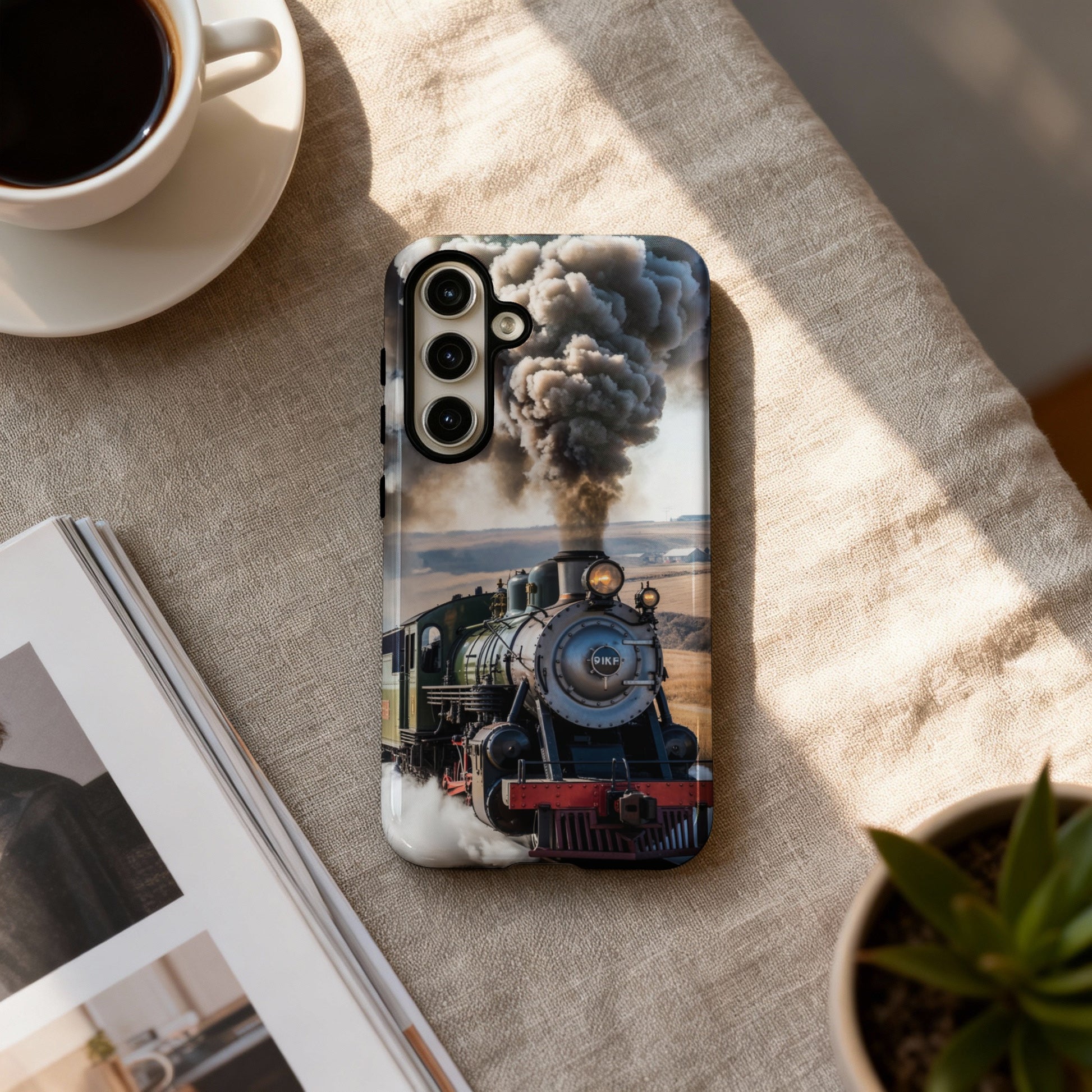 Smartphone case featuring a vintage steam train puffing smoke, with a coffee cup and plant nearby.