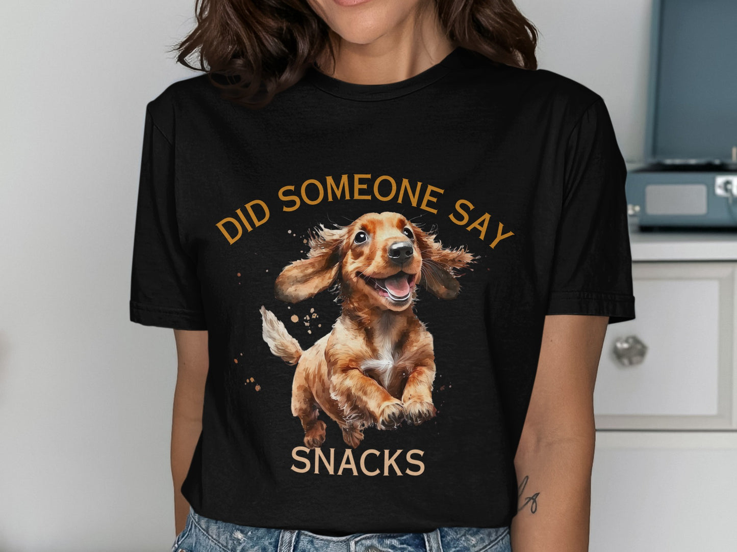 Dachshund wearing a t-shirt with "DID SOMEONE SAY SNACKS" text.