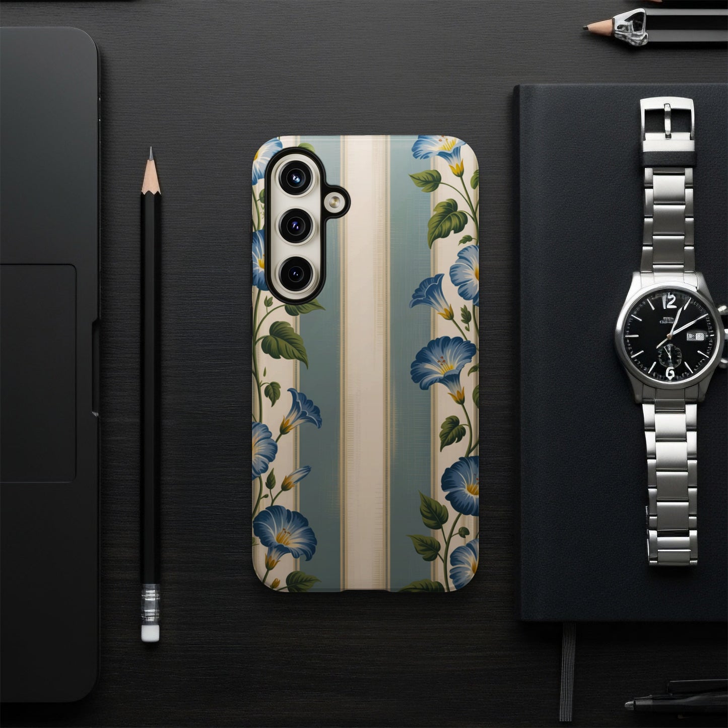 Phone case with blue floral print on striped background, next to watch and laptop.