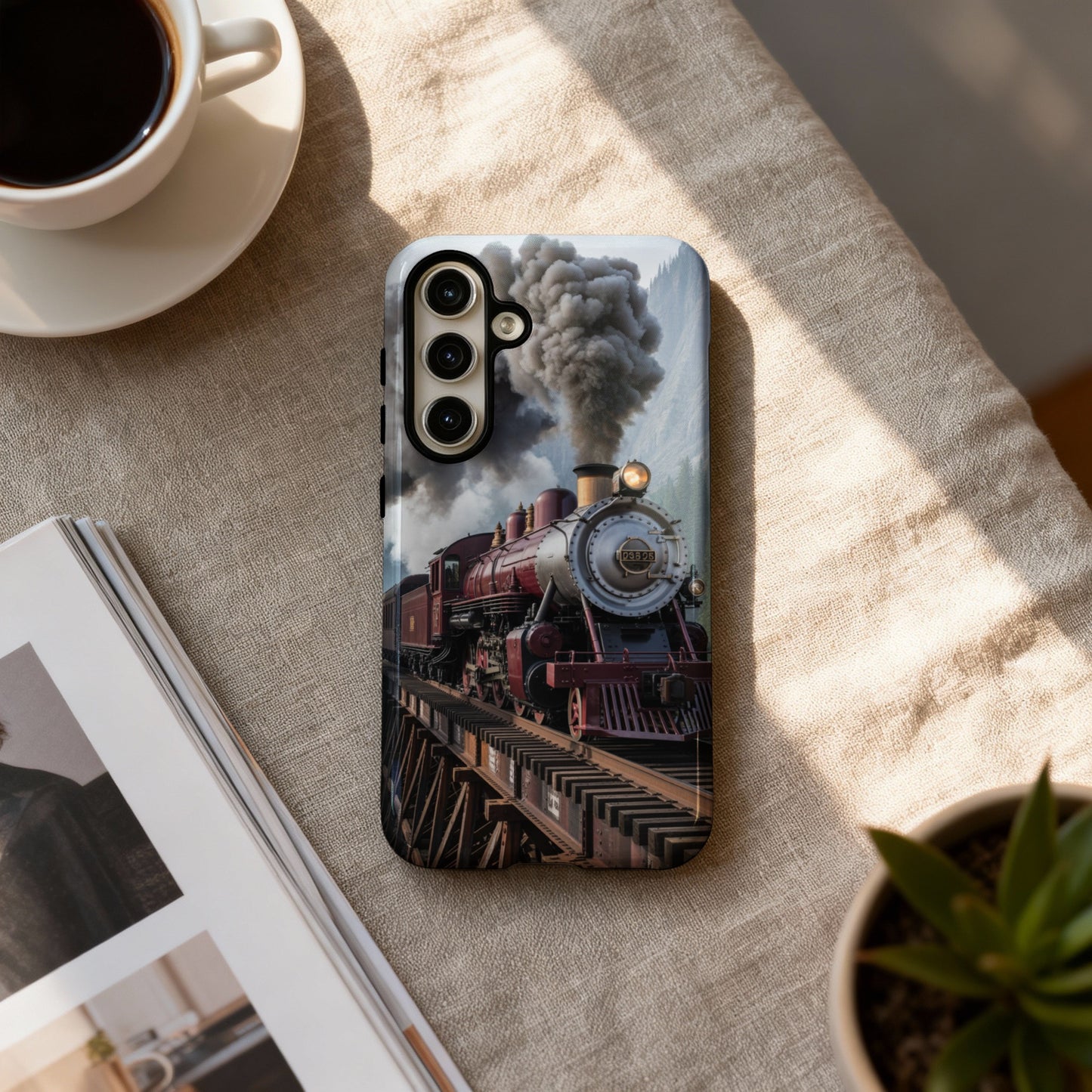 Phone case with a vintage steam train on a bridge, coffee, and plant.
