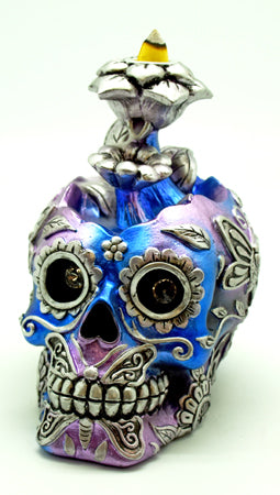 Decorative skull with blue and purple hues, silver embellishments, and a small figure on top against a white background.