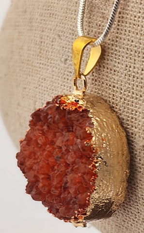 Gold pendant with a red stone on a beige fabric background