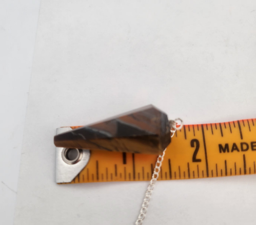 Crystal pendant with chain on a ruler for scale against a white background