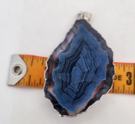 Blue agate pendant with a ruler for scale on a white background