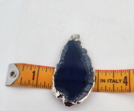 Blue geode pendant with silver edge on a white background with a measuring tape for scale.