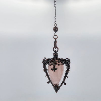 Decorative pendant with pink stone and intricate metalwork on a white background
