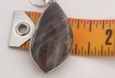 Teardrop-shaped stone pendant with silver setting on a ruler for scale