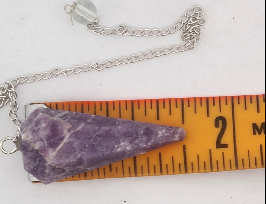 Purple crystal pendant on a chain with a ruler for scale on a white background