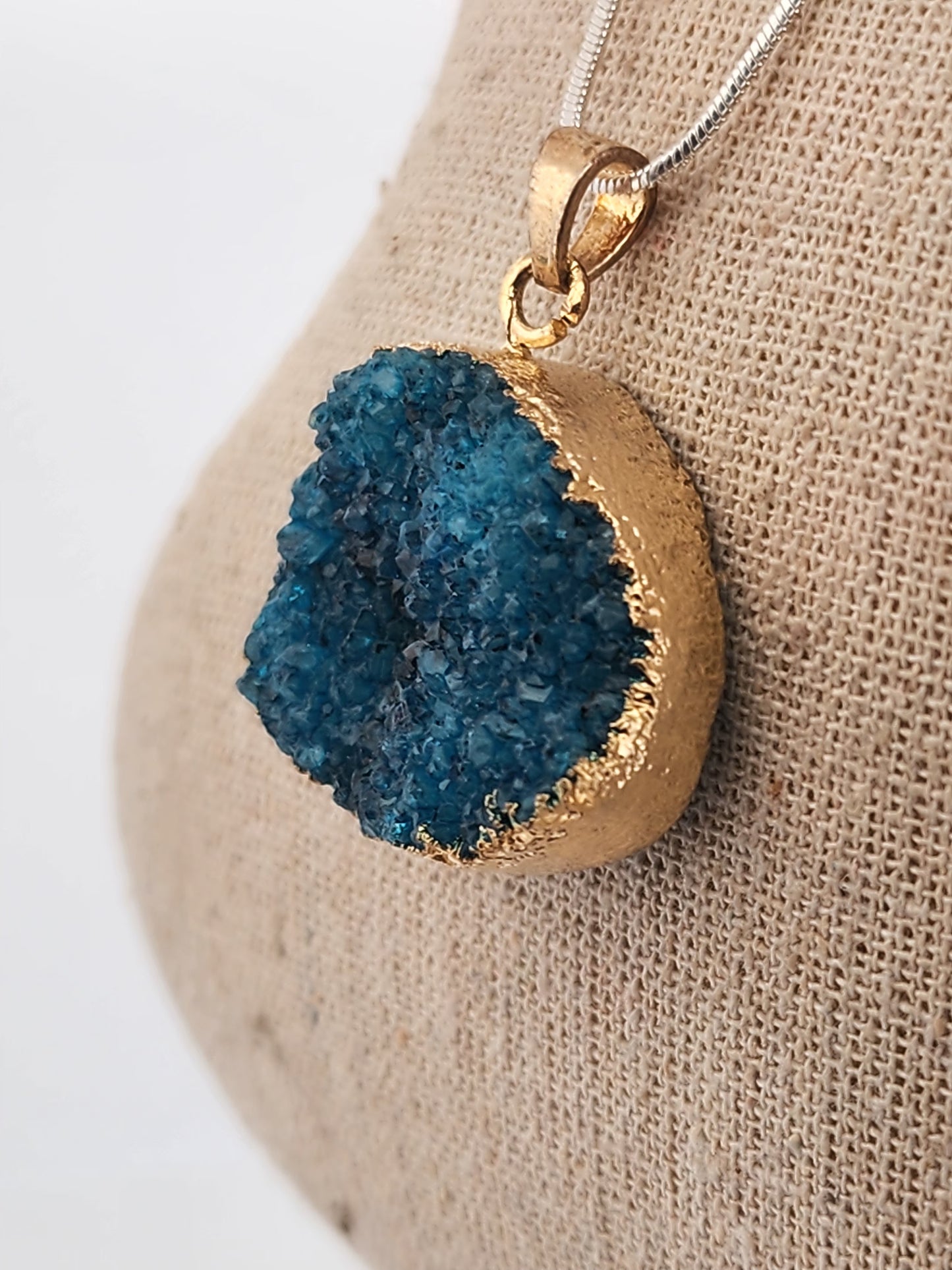 Gold pendant with blue geode on a beige fabric background