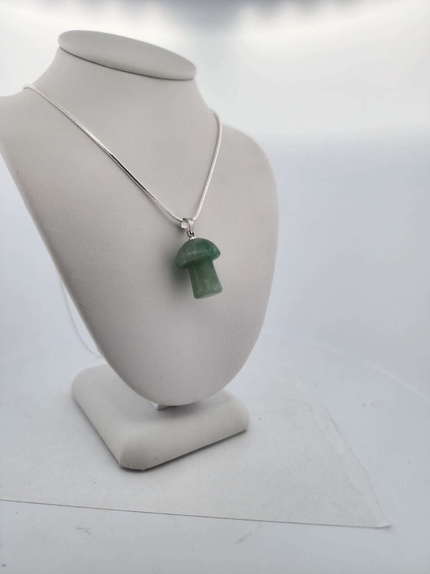 Green mushroom-shaped pendant on a silver chain displayed on a gray bust