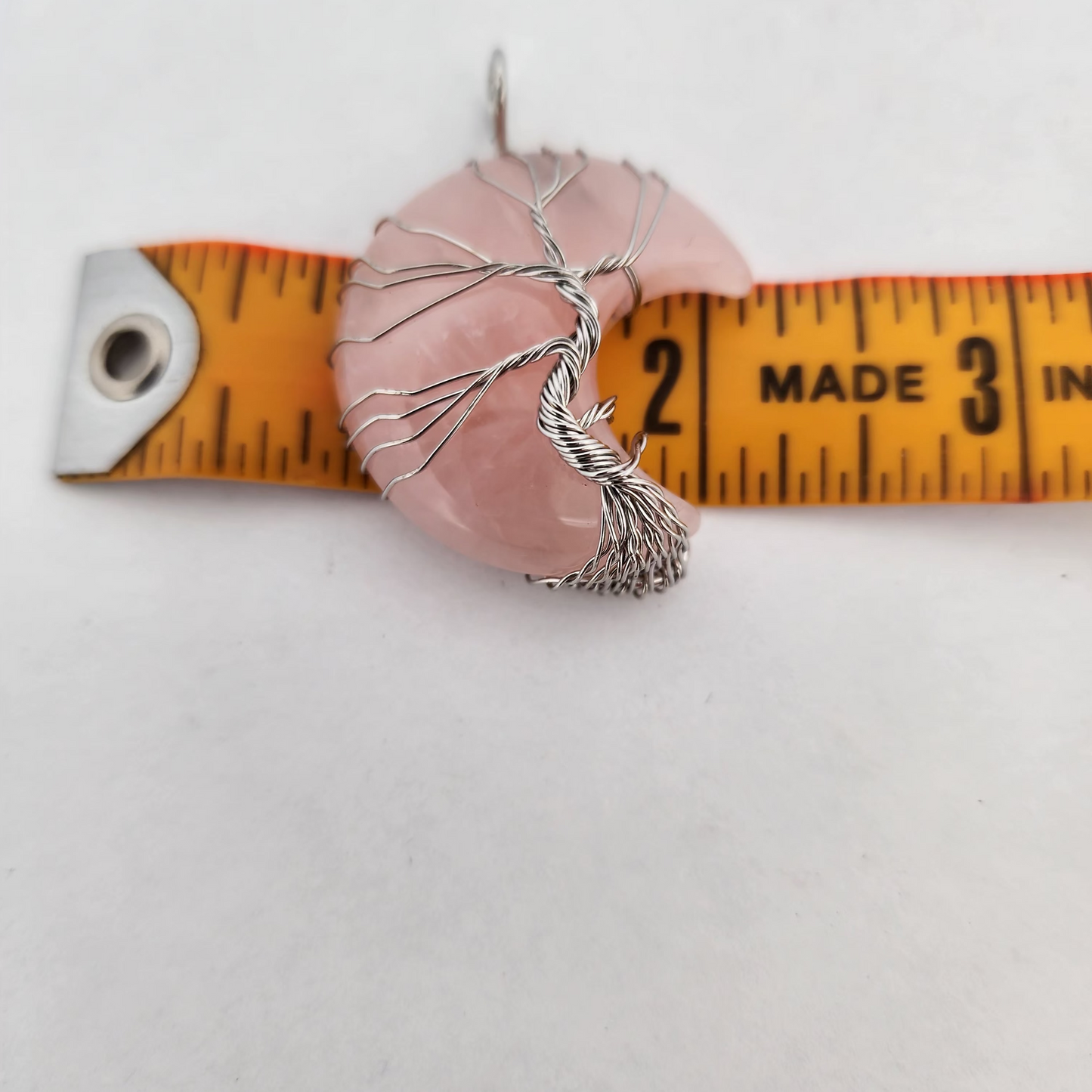 Pink stone pendant with silver tree design on a white background with a measuring tape.