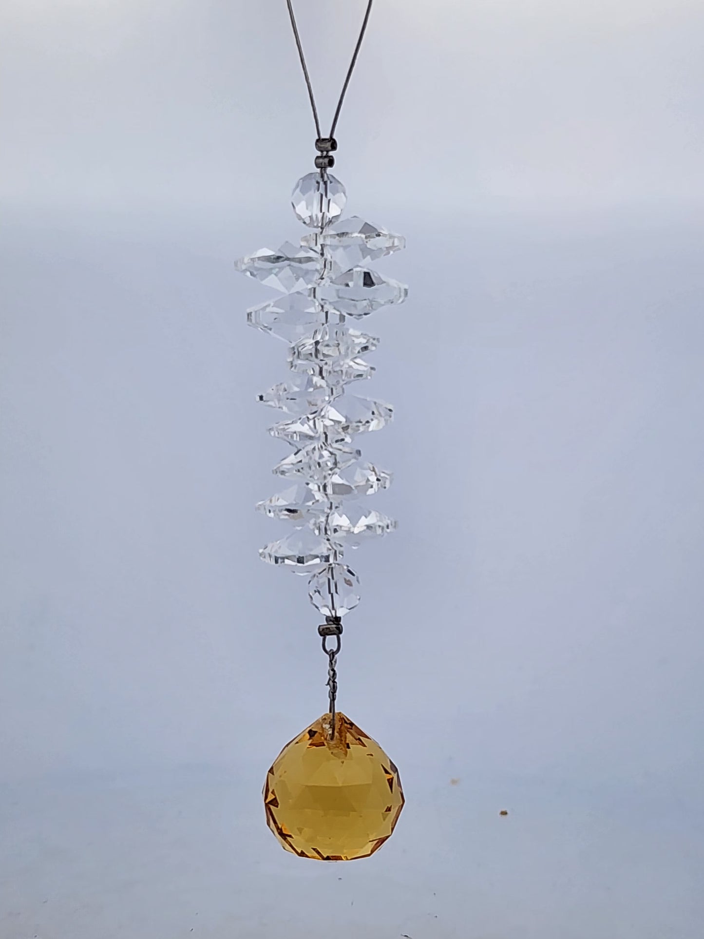 Crystal hanging ornament with a yellow gemstone on a plain background
