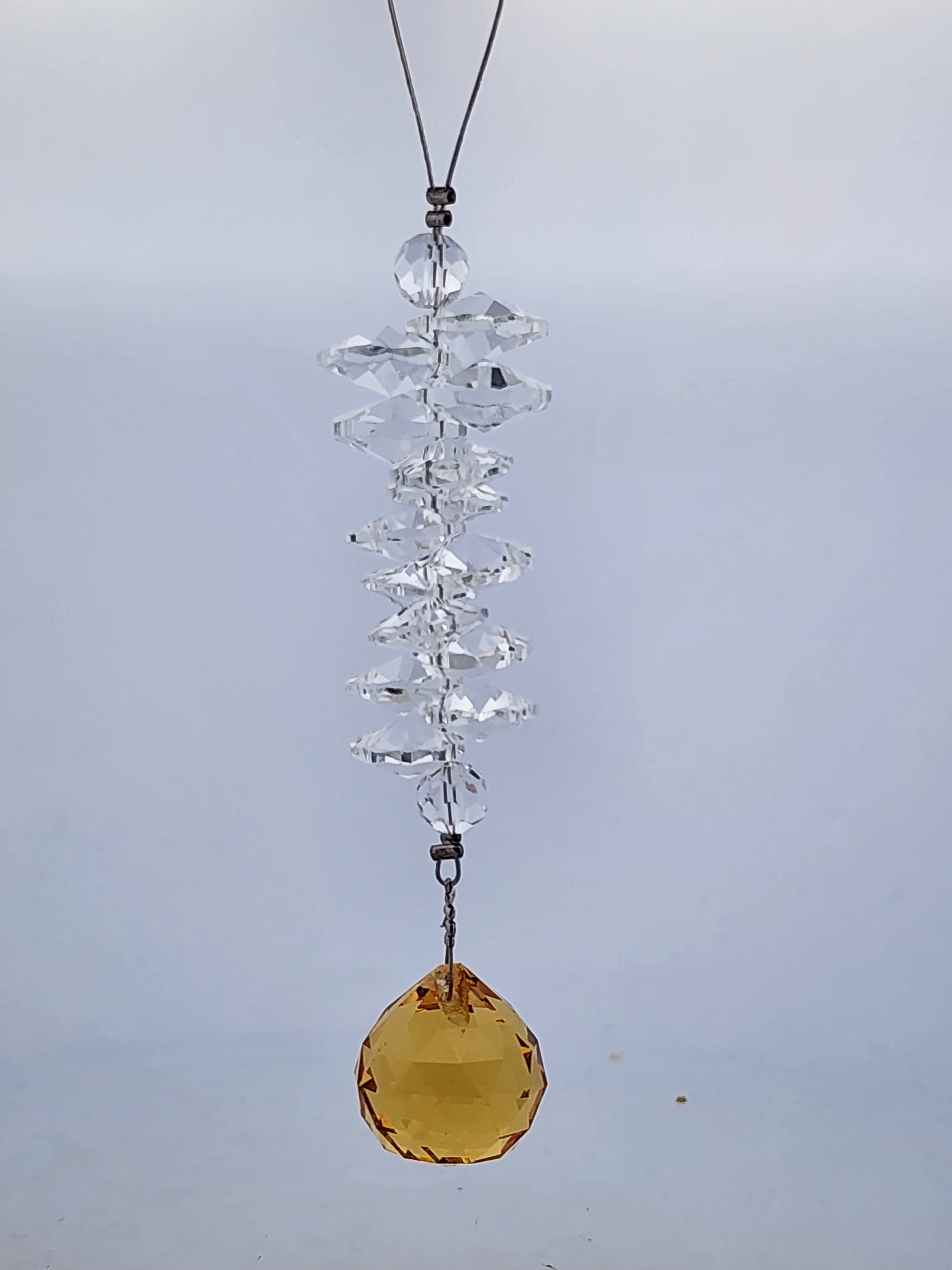 Crystal hanging ornament with a yellow gemstone on a plain background