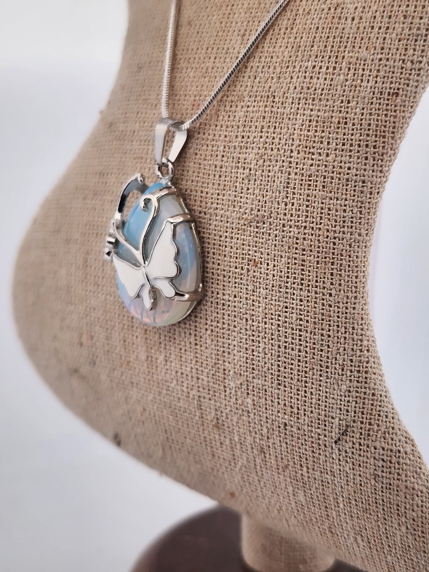 Butterfly-shaped pendant on a chain displayed on a burlap surface.
