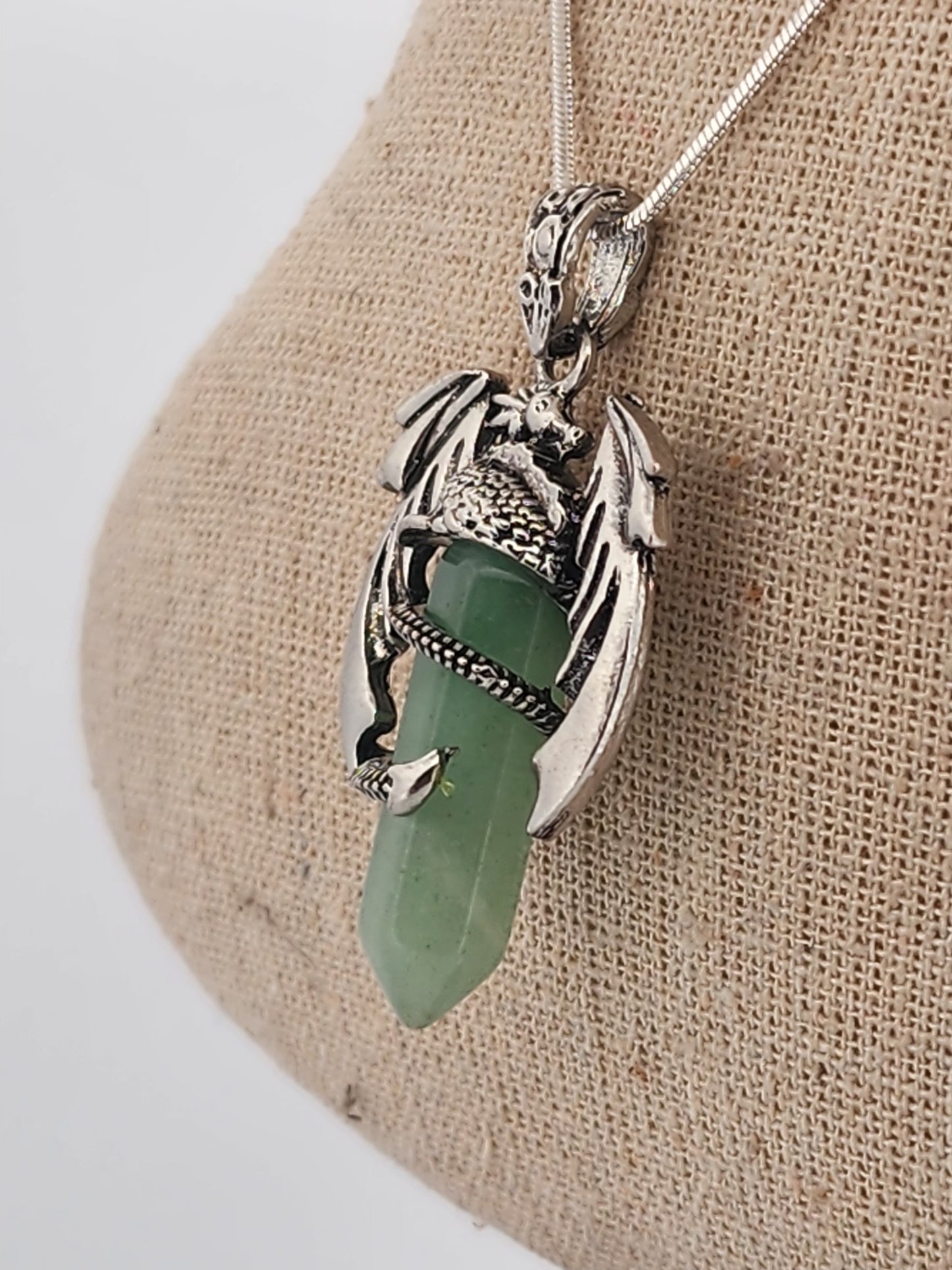 Silver pendant with green stone on a beige fabric background
