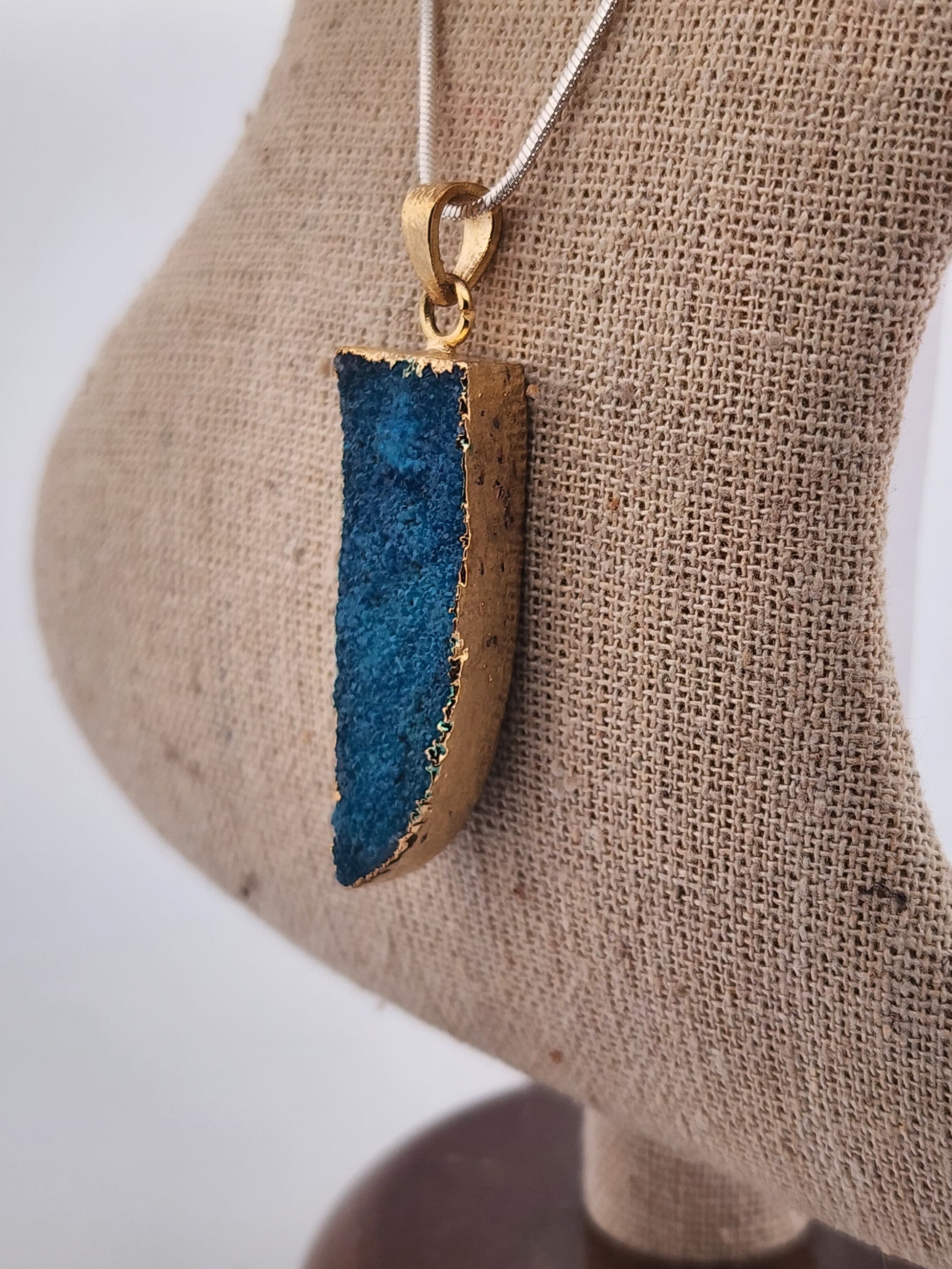 Blue and gold pendant on a mannequin bust with a neutral background