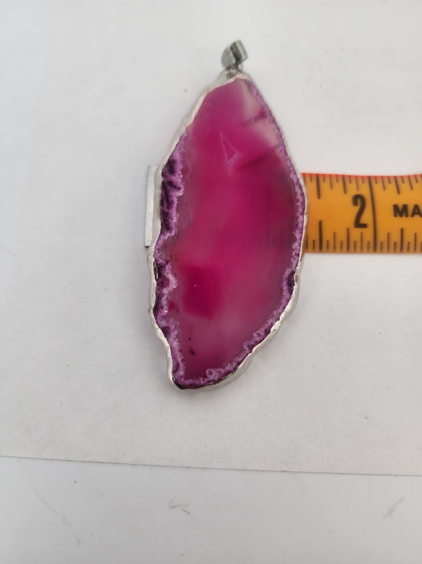 Pink agate pendant with silver setting on a white background, measured by a ruler.