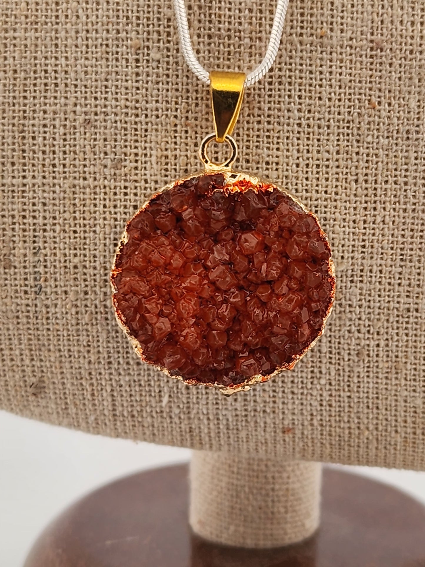 Round brown pendant on a gold chain against a beige fabric background