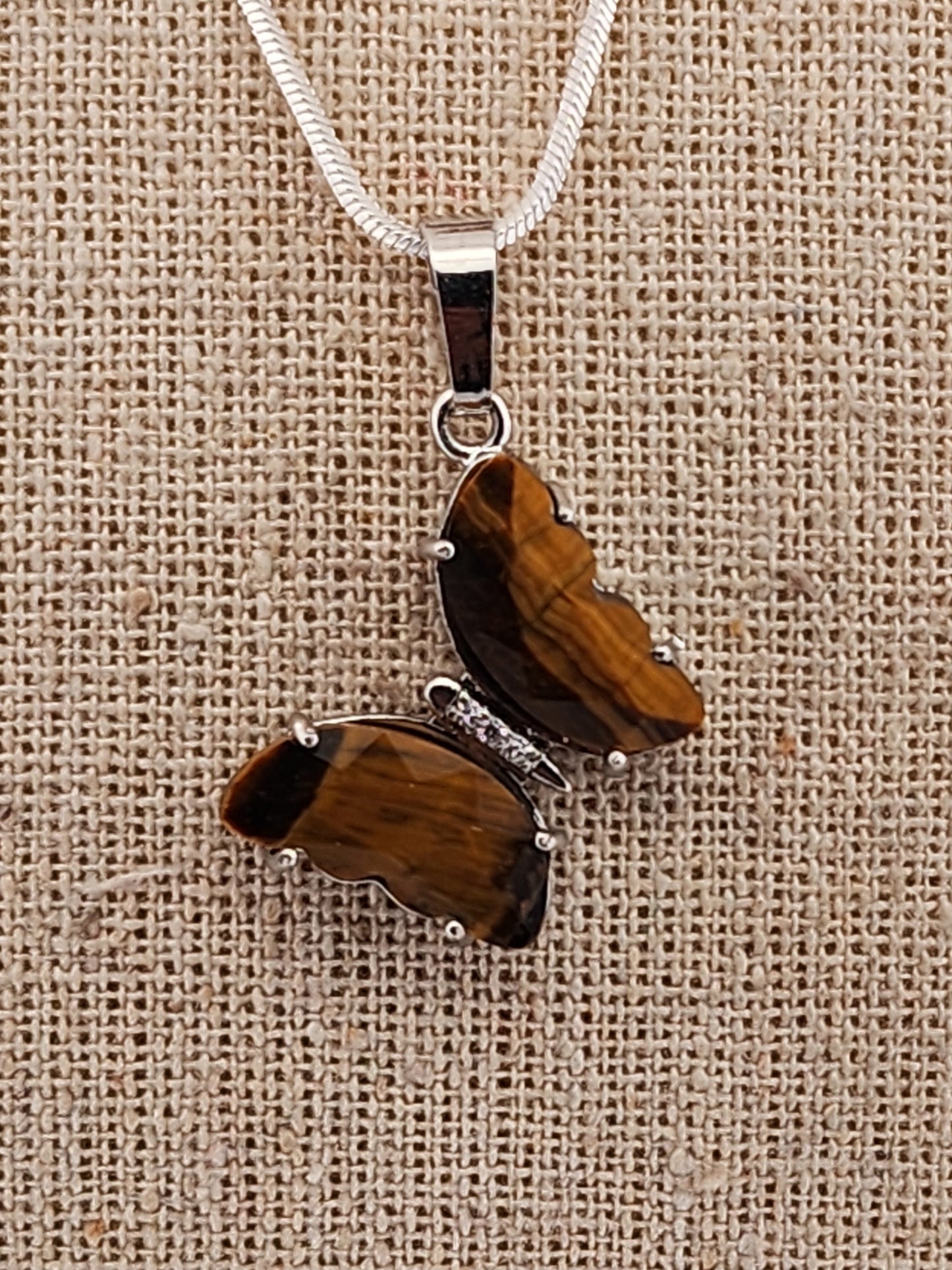 Butterfly-shaped pendant with wooden texture on a beige fabric background