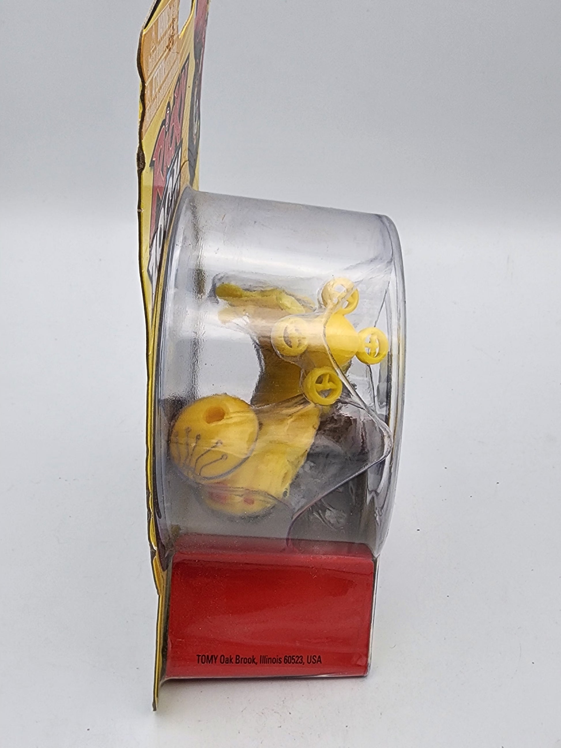 Yellow toy figure in a transparent box with a red base on a white background