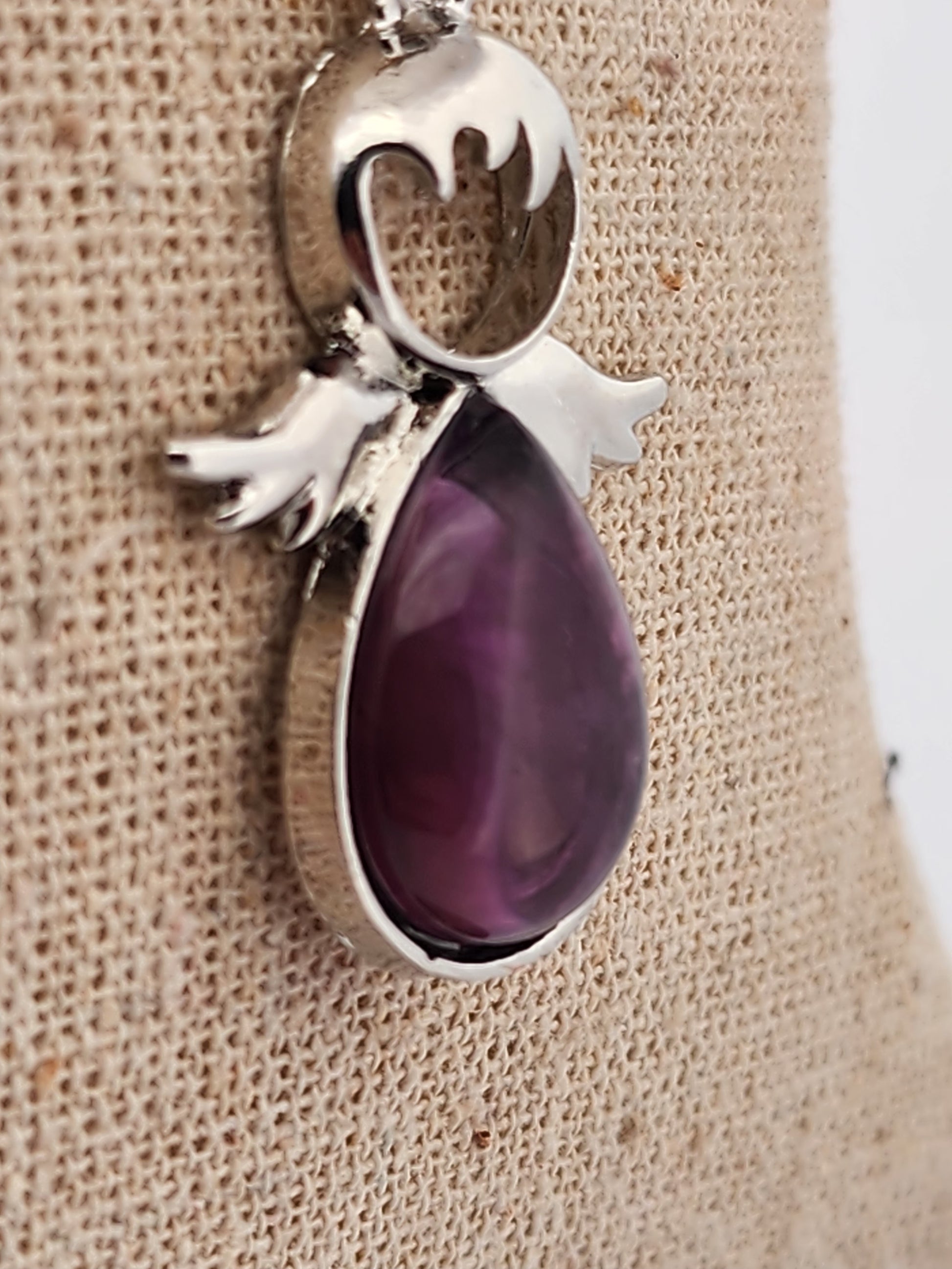 Silver pendant with a purple teardrop-shaped gemstone on a textured beige background