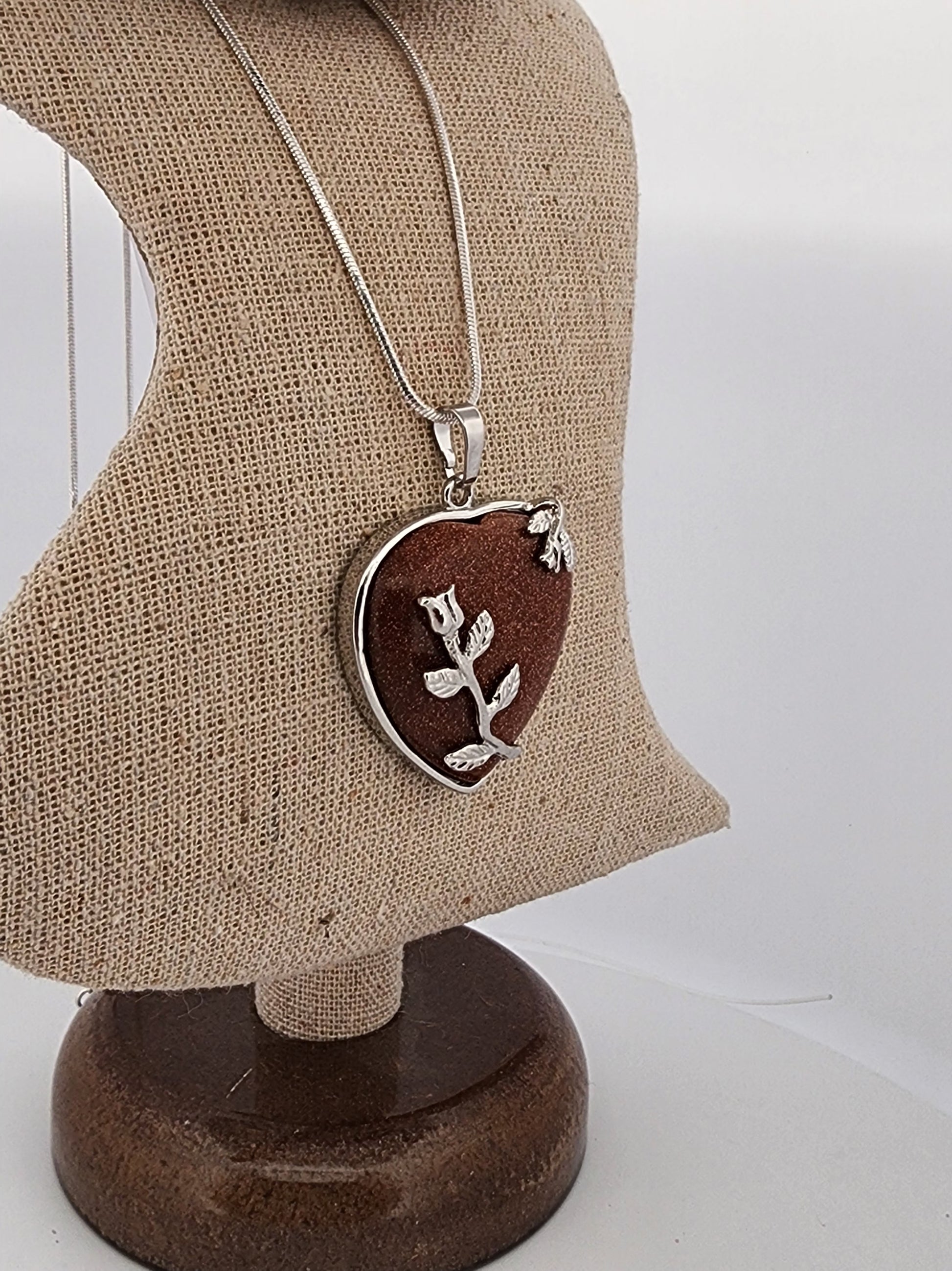 Necklace with a heart-shaped pendant featuring a floral design on a mannequin bust.