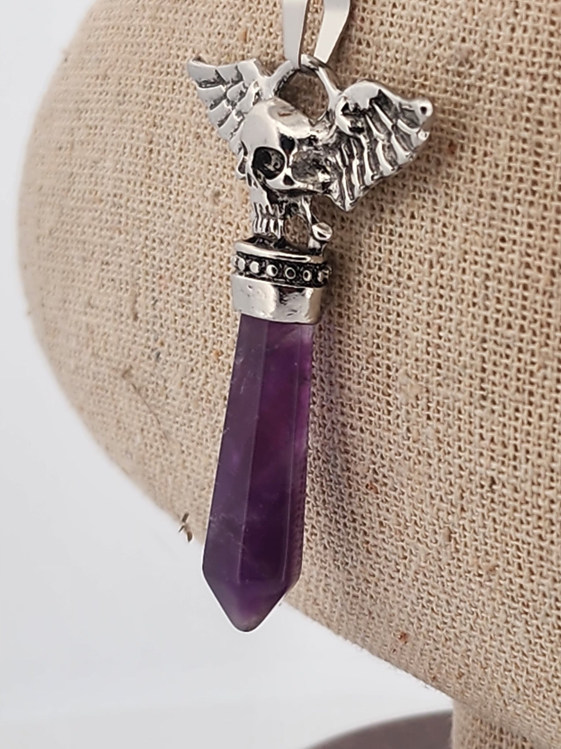 Silver skull pendant with purple crystal on a beige fabric background