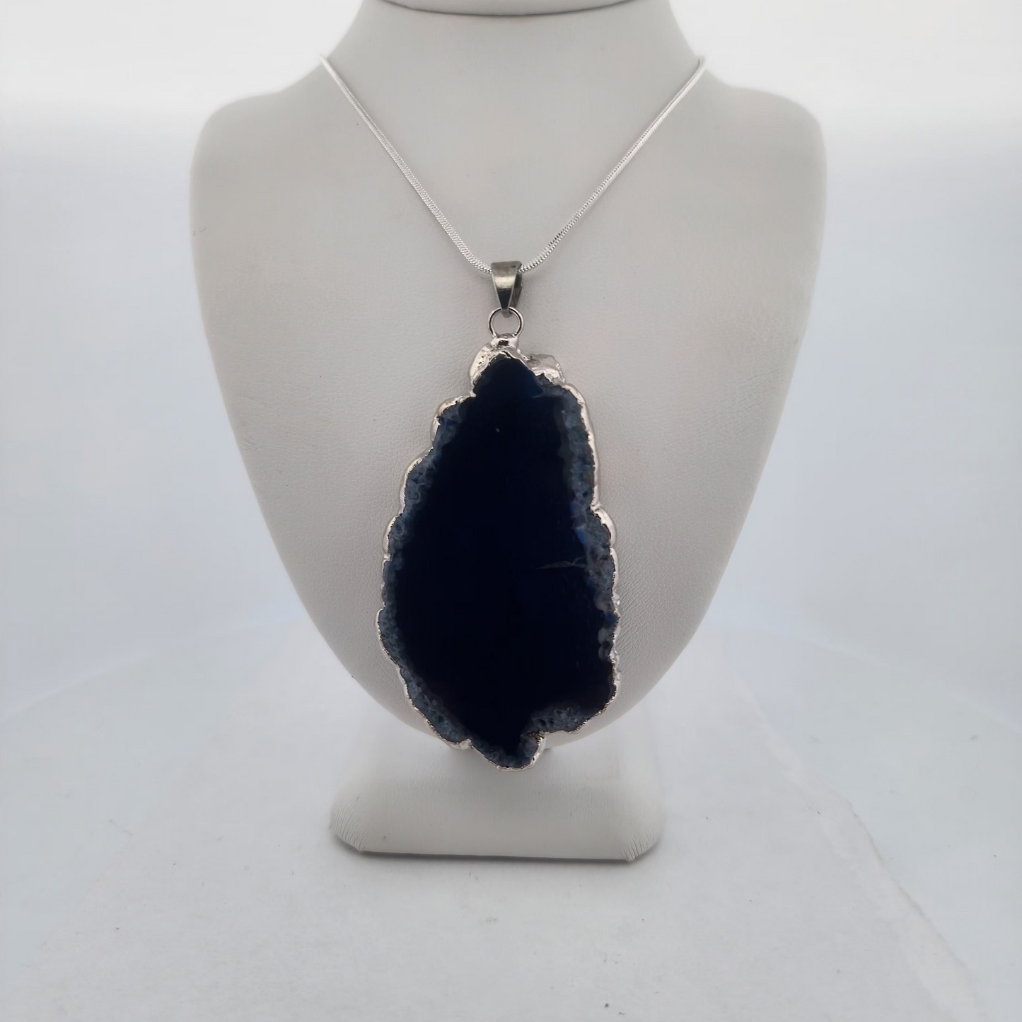Navy blue stone pendant on a white mannequin bust against a white background