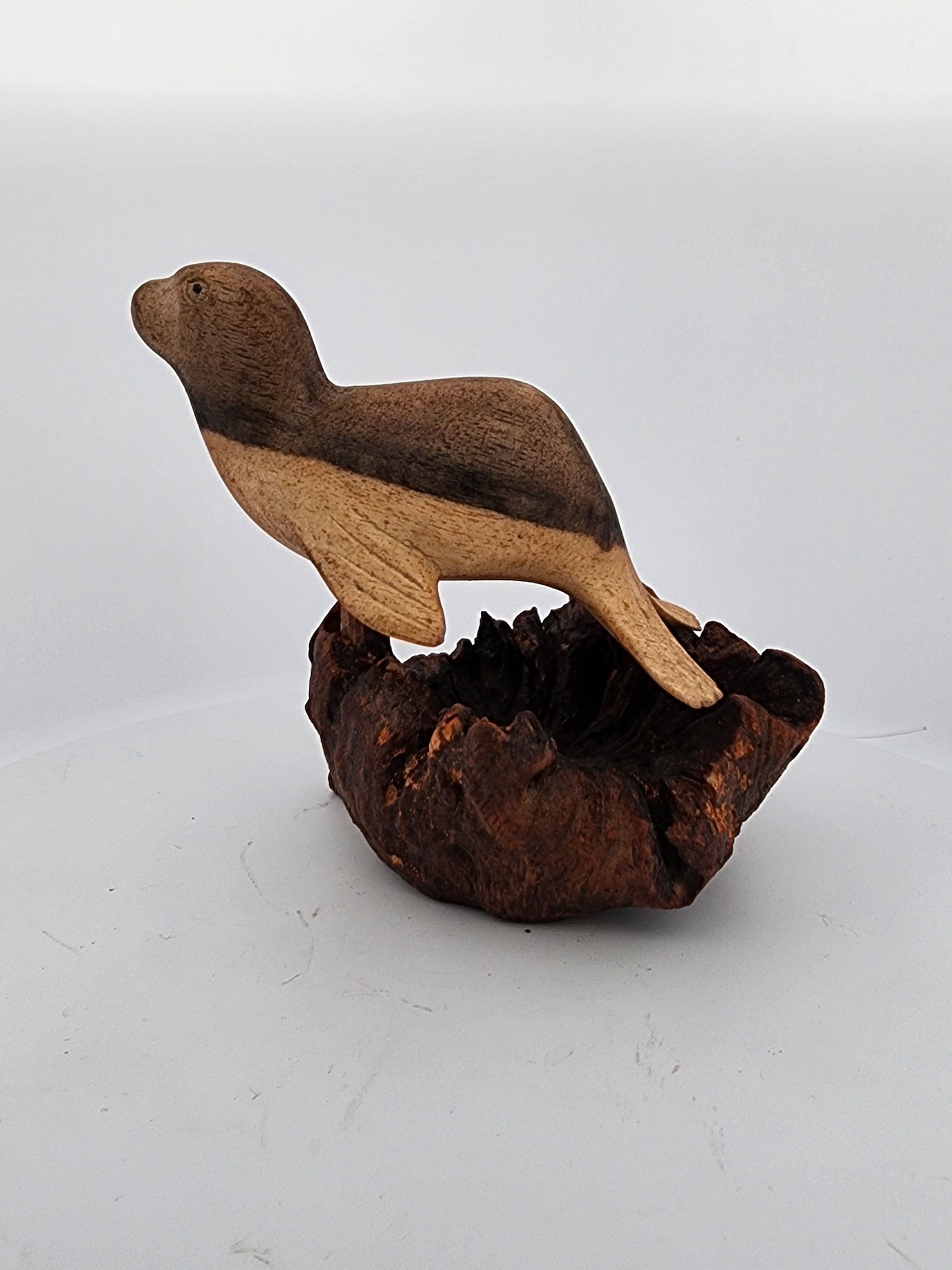 Wooden bird figurine perched on a textured brown base against a white background