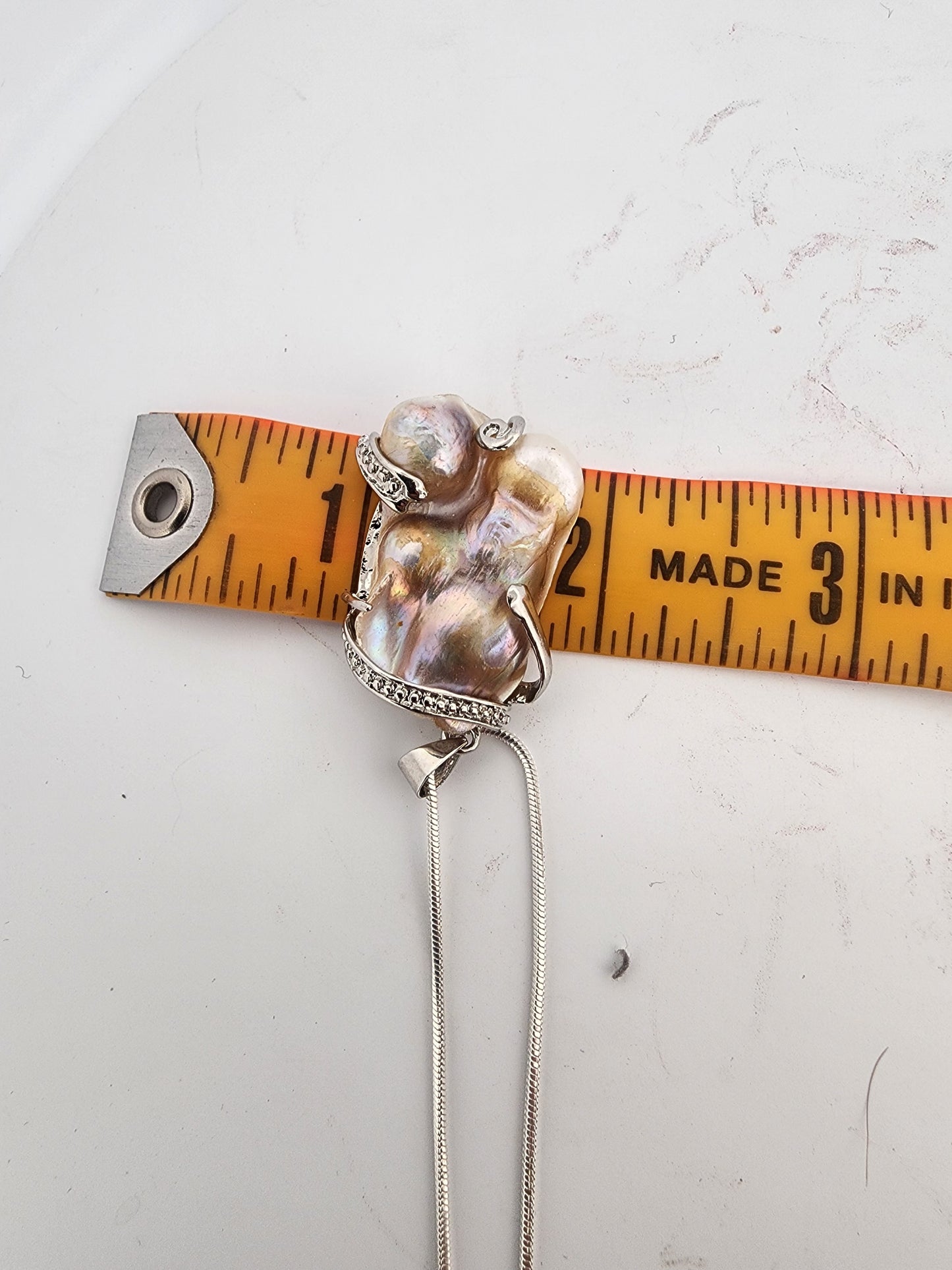 Necklace with a pendant being measured against a ruler on a white surface
