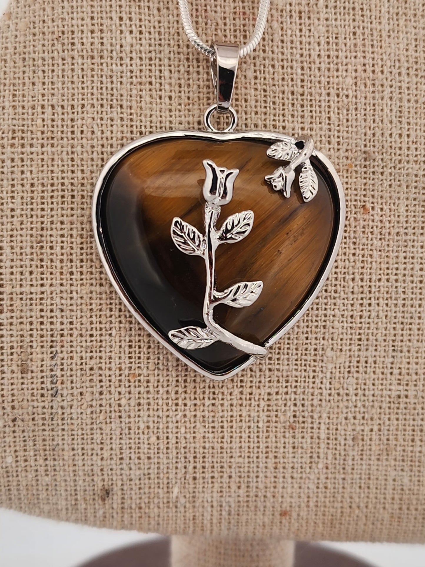 Heart-shaped pendant with rose design on a brown fabric background