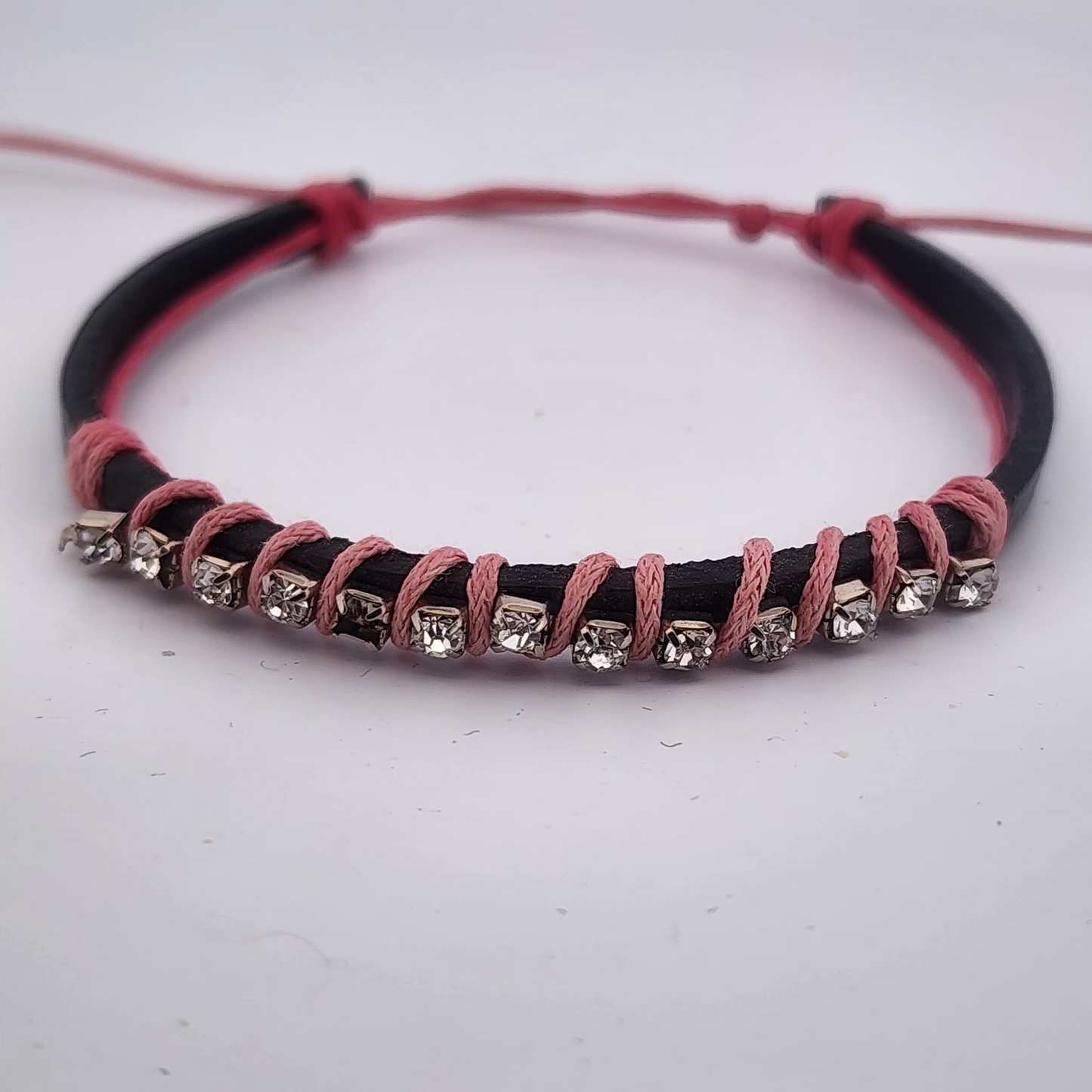 Bracelet with black and pink cord and small crystals on a white background
