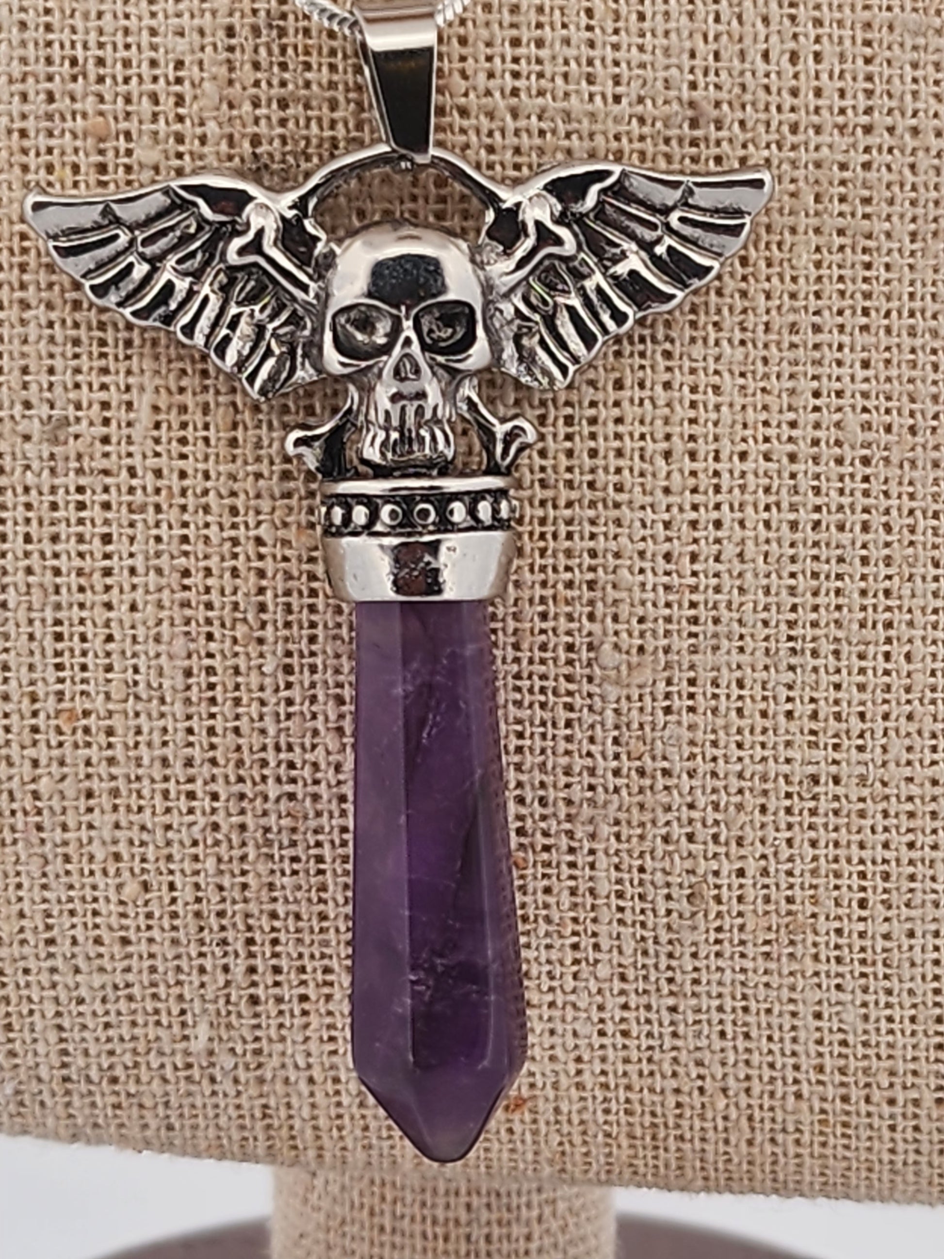 Pendant with skull design and purple crystal on a textured beige background