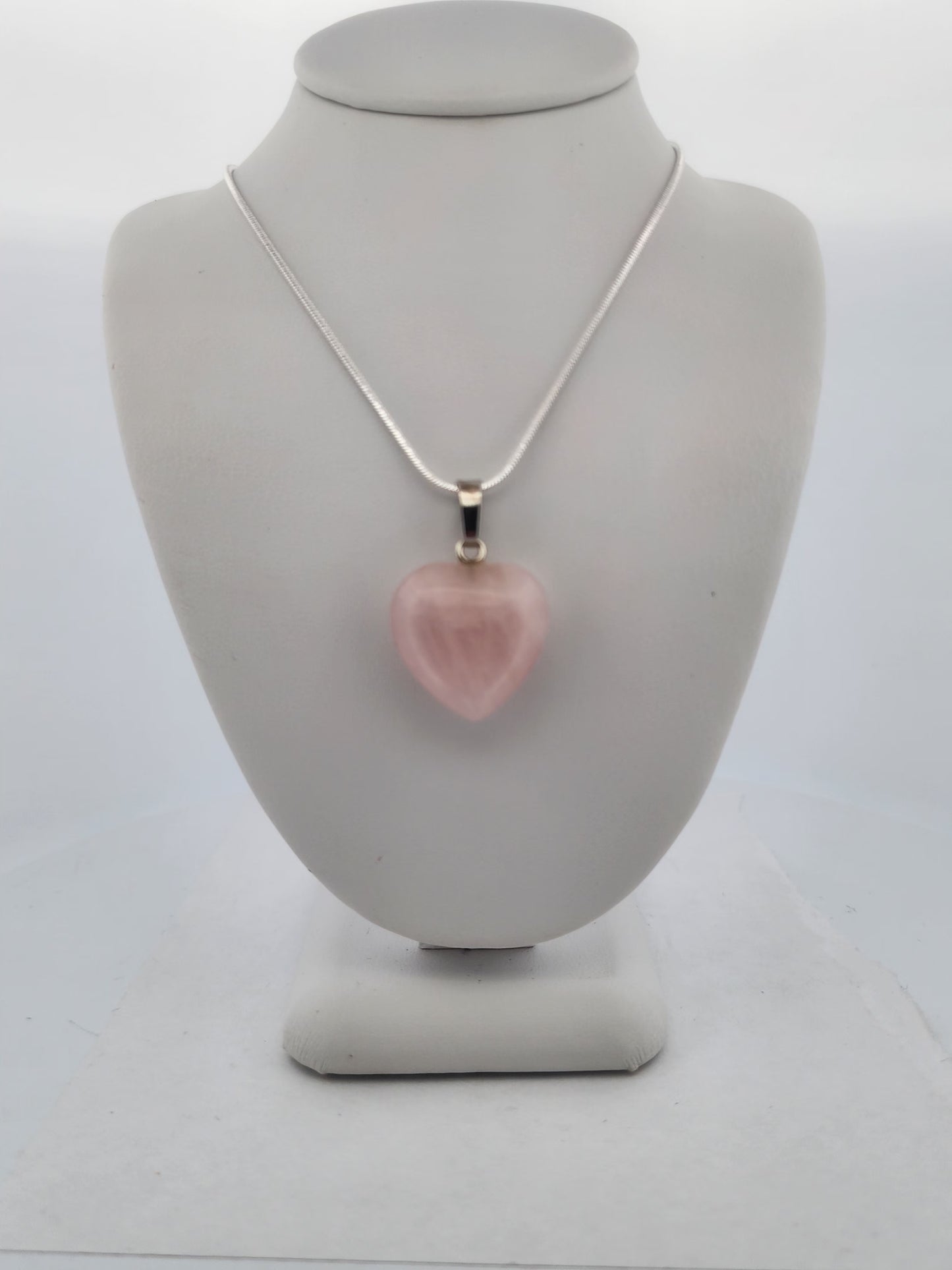 Necklace with a pink heart-shaped pendant on a gray mannequin bust.