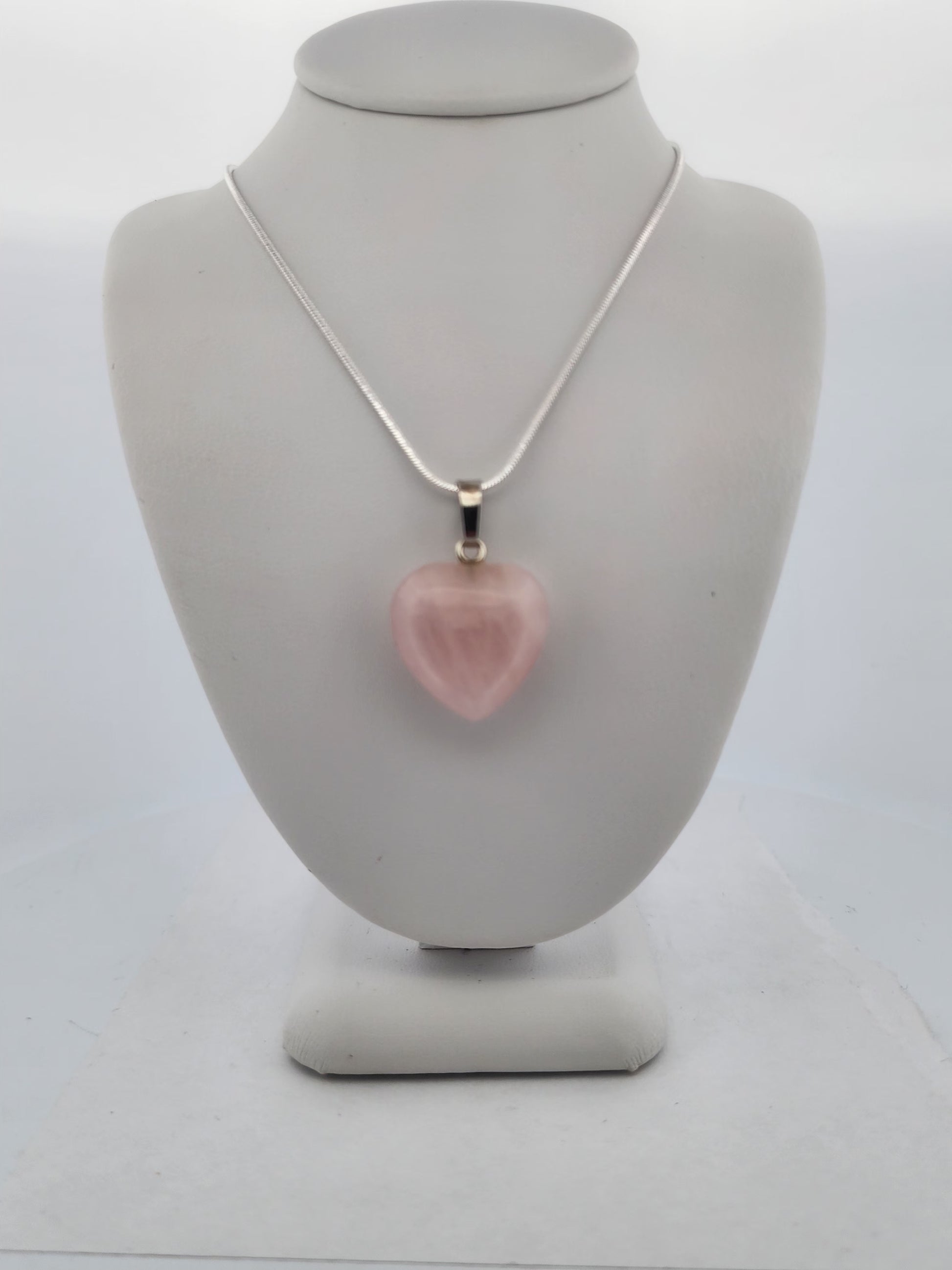 Necklace with a pink heart-shaped pendant on a gray mannequin bust.