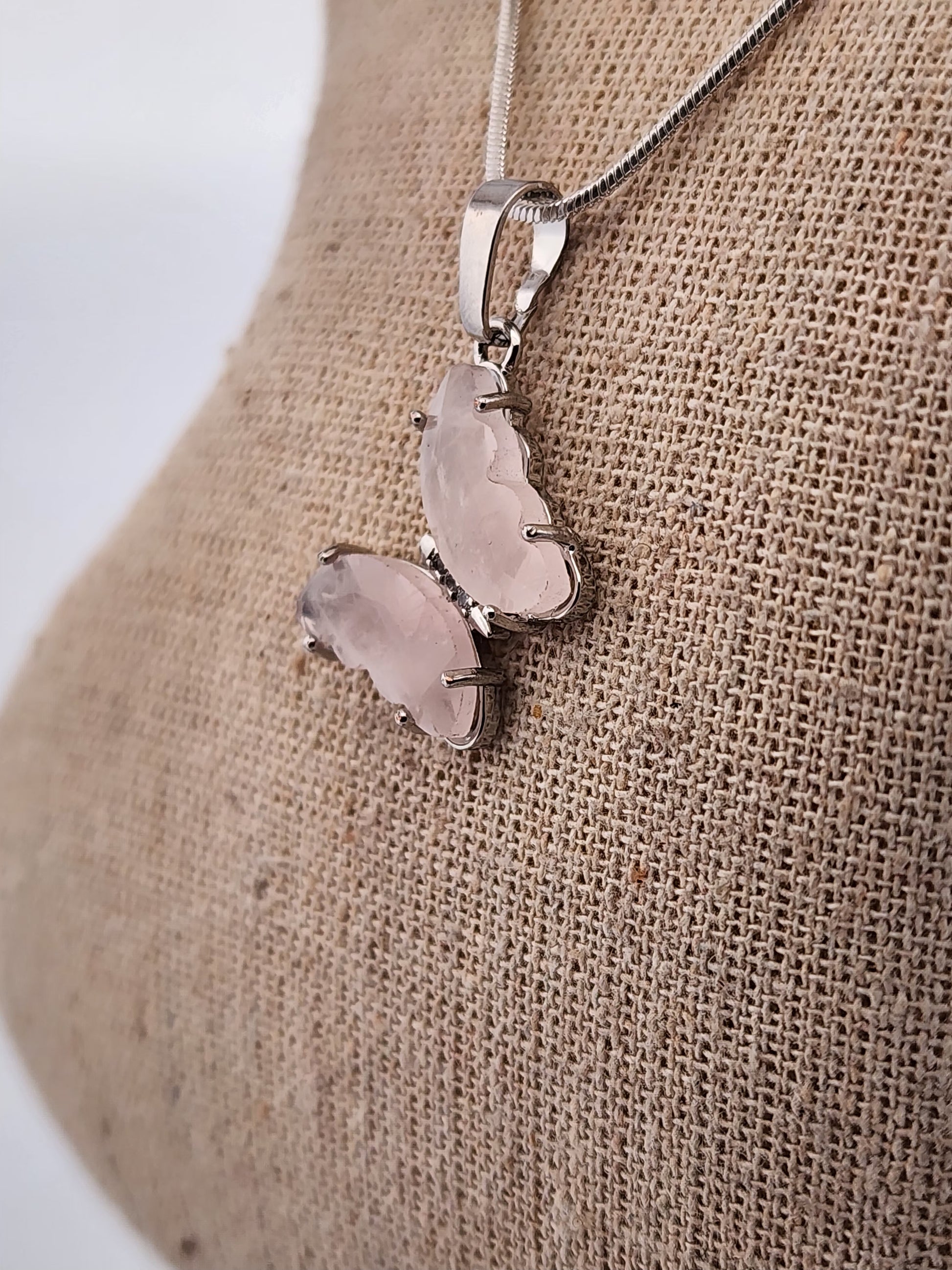 Butterfly-shaped pendant on a chain against a textured beige background