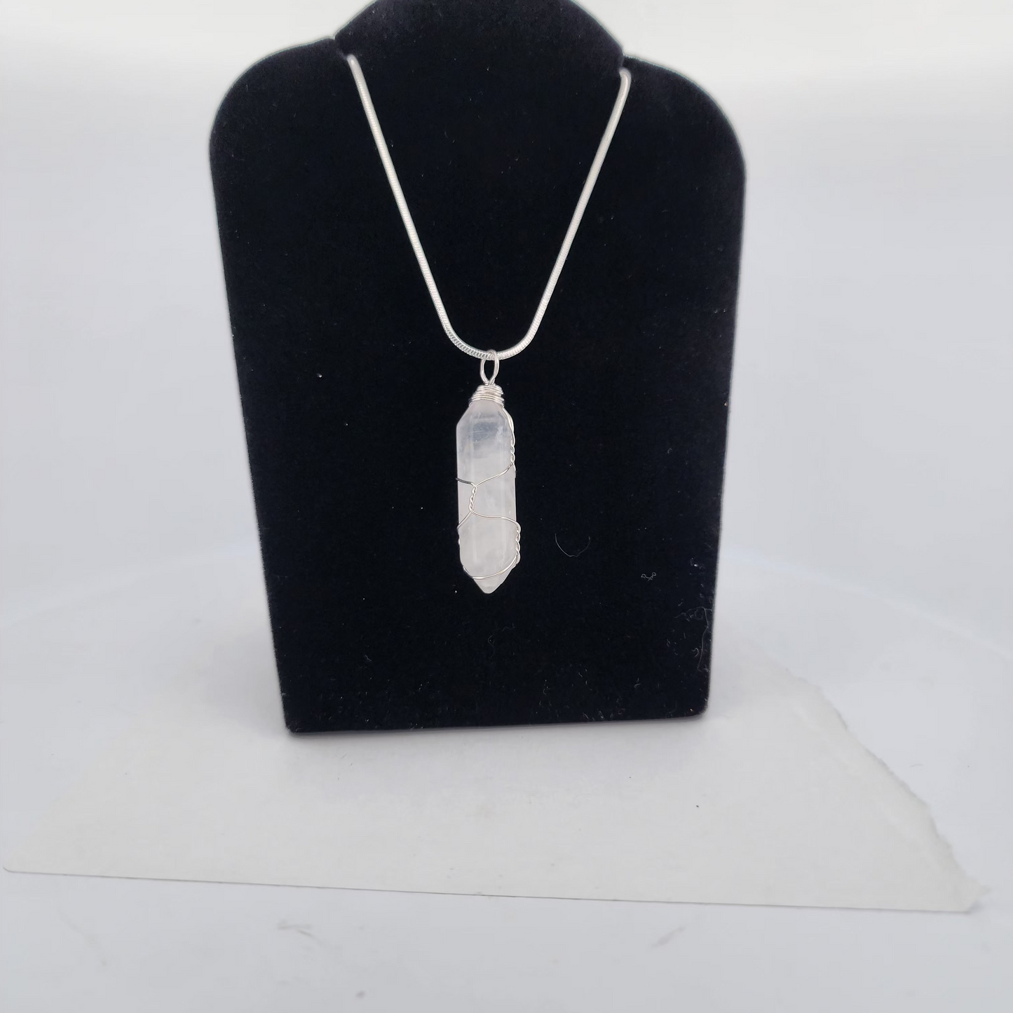 Silver necklace with a pendant on a black velvet stand against a white background