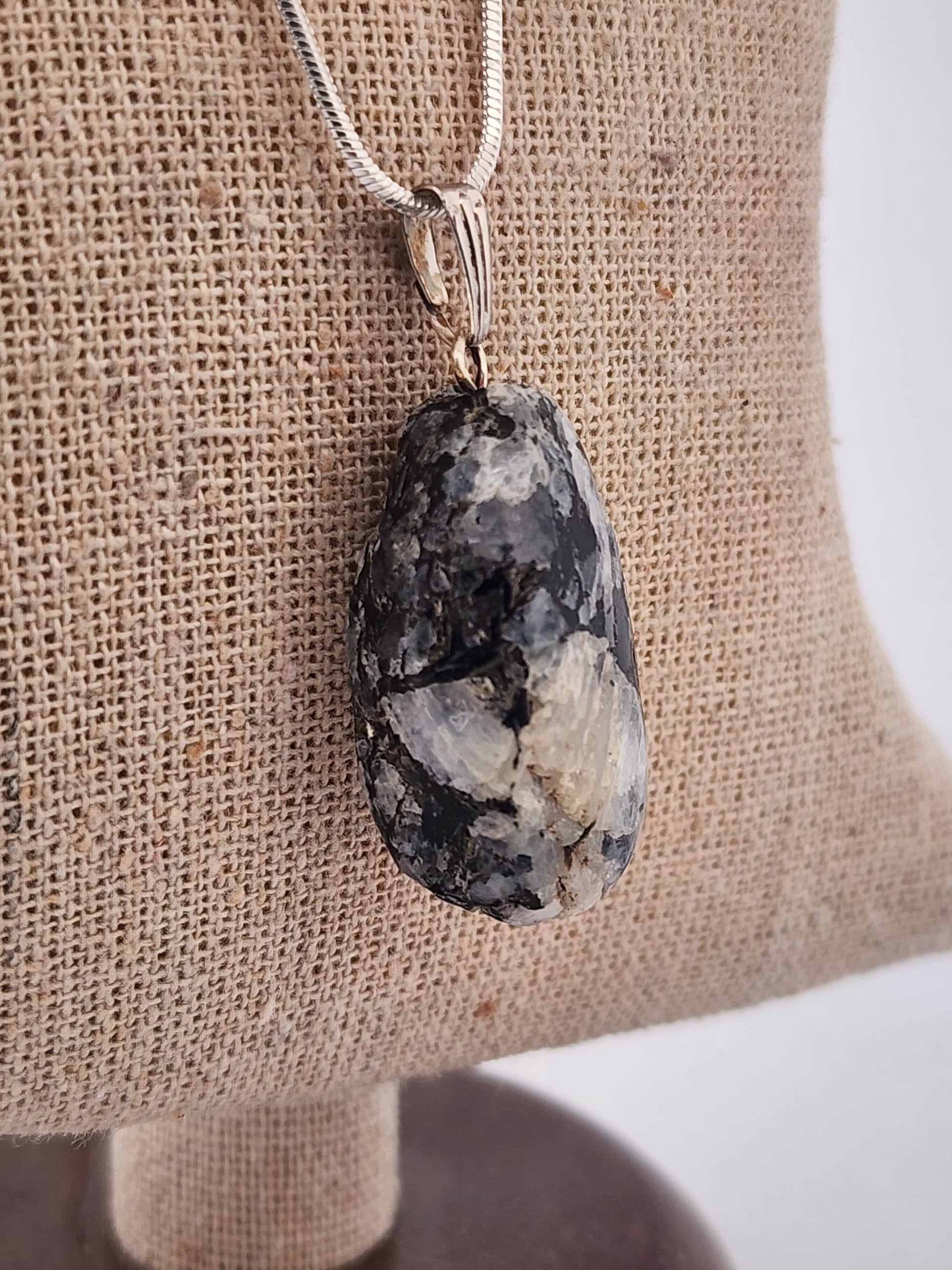 Necklace with a large, rough-textured stone pendant on a burlap surface.