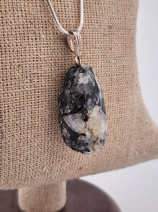 Necklace with a large, rough-textured stone pendant on a burlap surface.