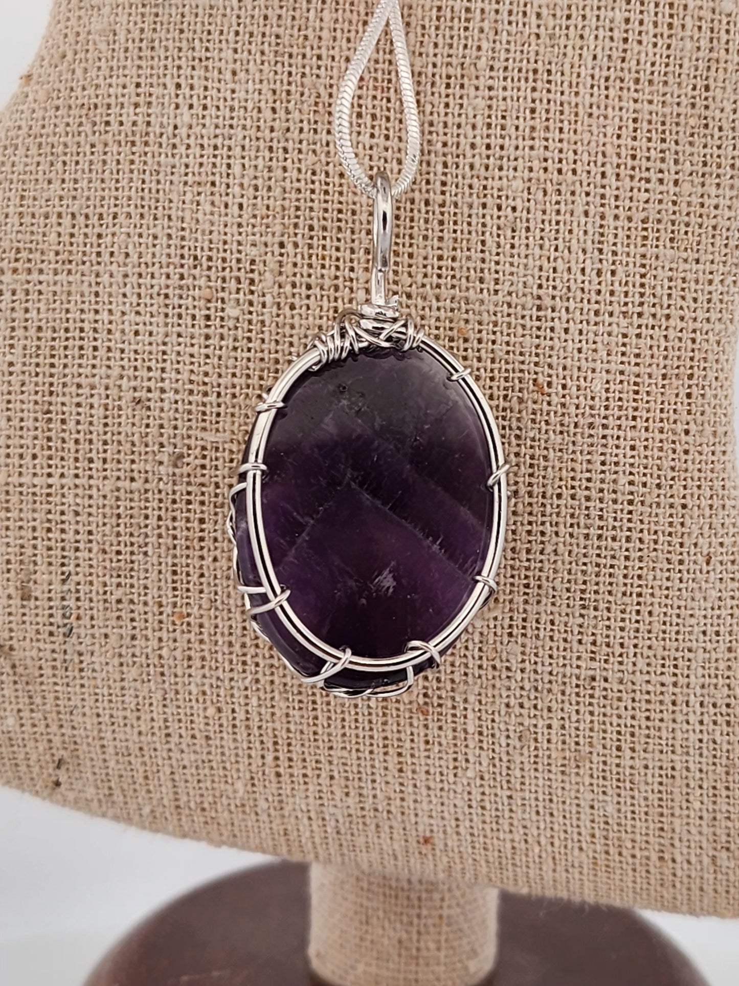 Amethyst pendant with silver wire wrapping on a beige fabric background