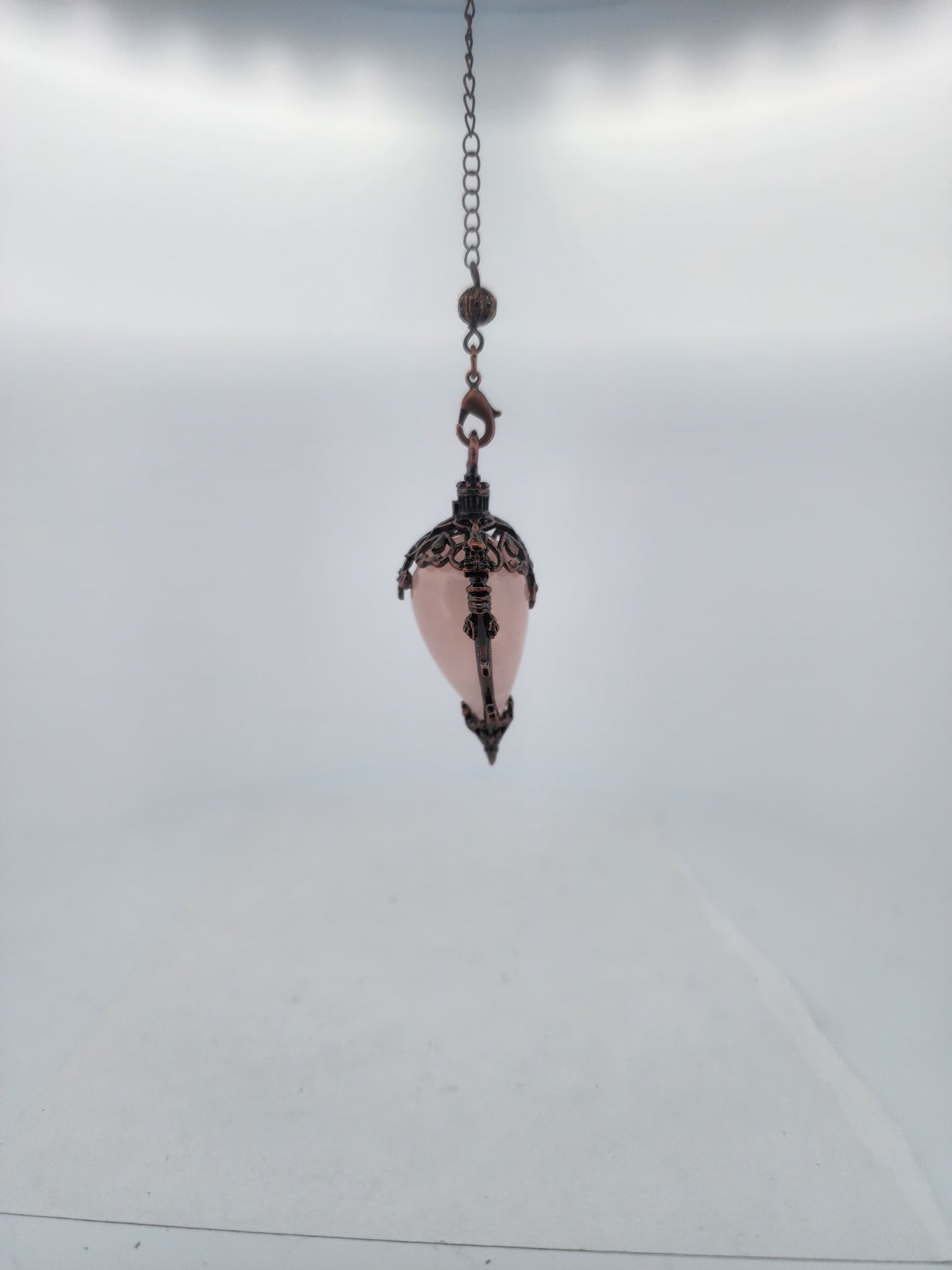 Decorative hanging pendant with pink glass and metal chain on a light gray background