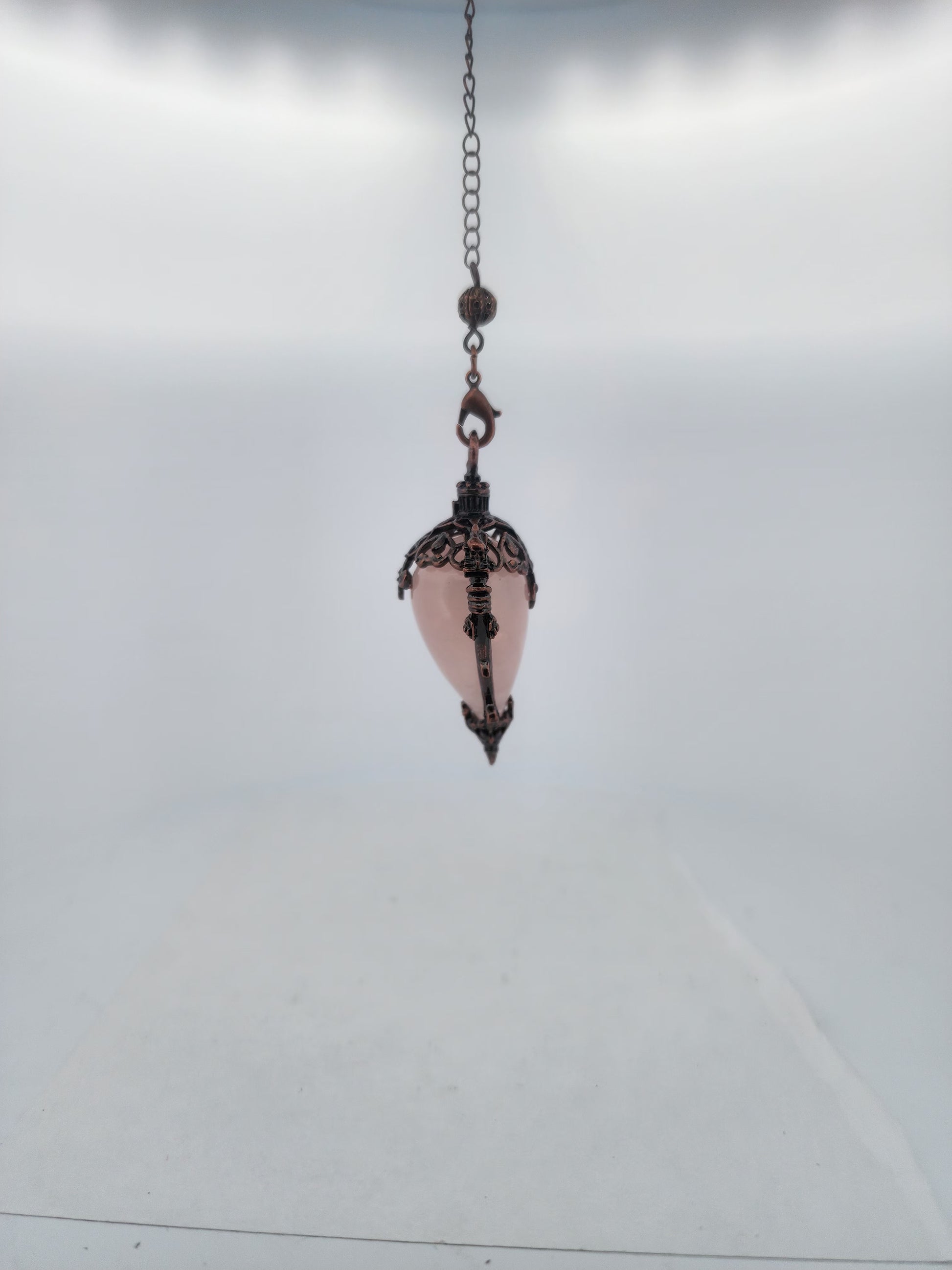 Decorative hanging pendant with pink glass and metal chain on a light gray background